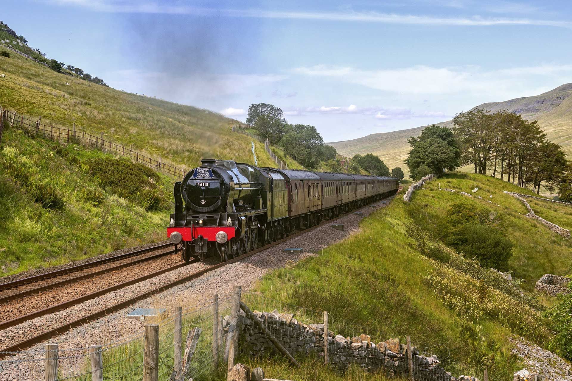Steam train traveling through a green valley, under a blue sky.