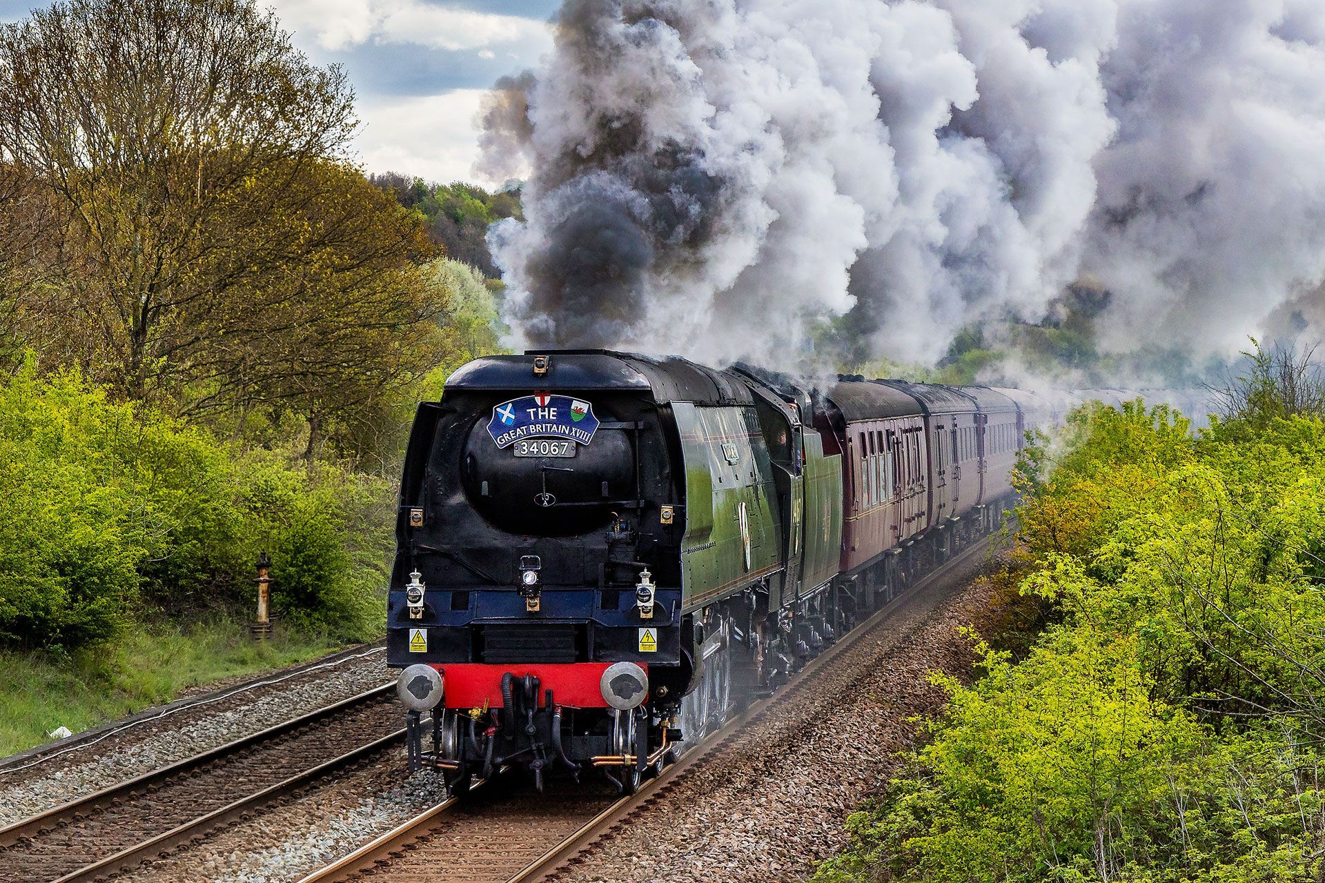 Steam locomotive hauling passenger cars through countryside, billowing thick white smoke