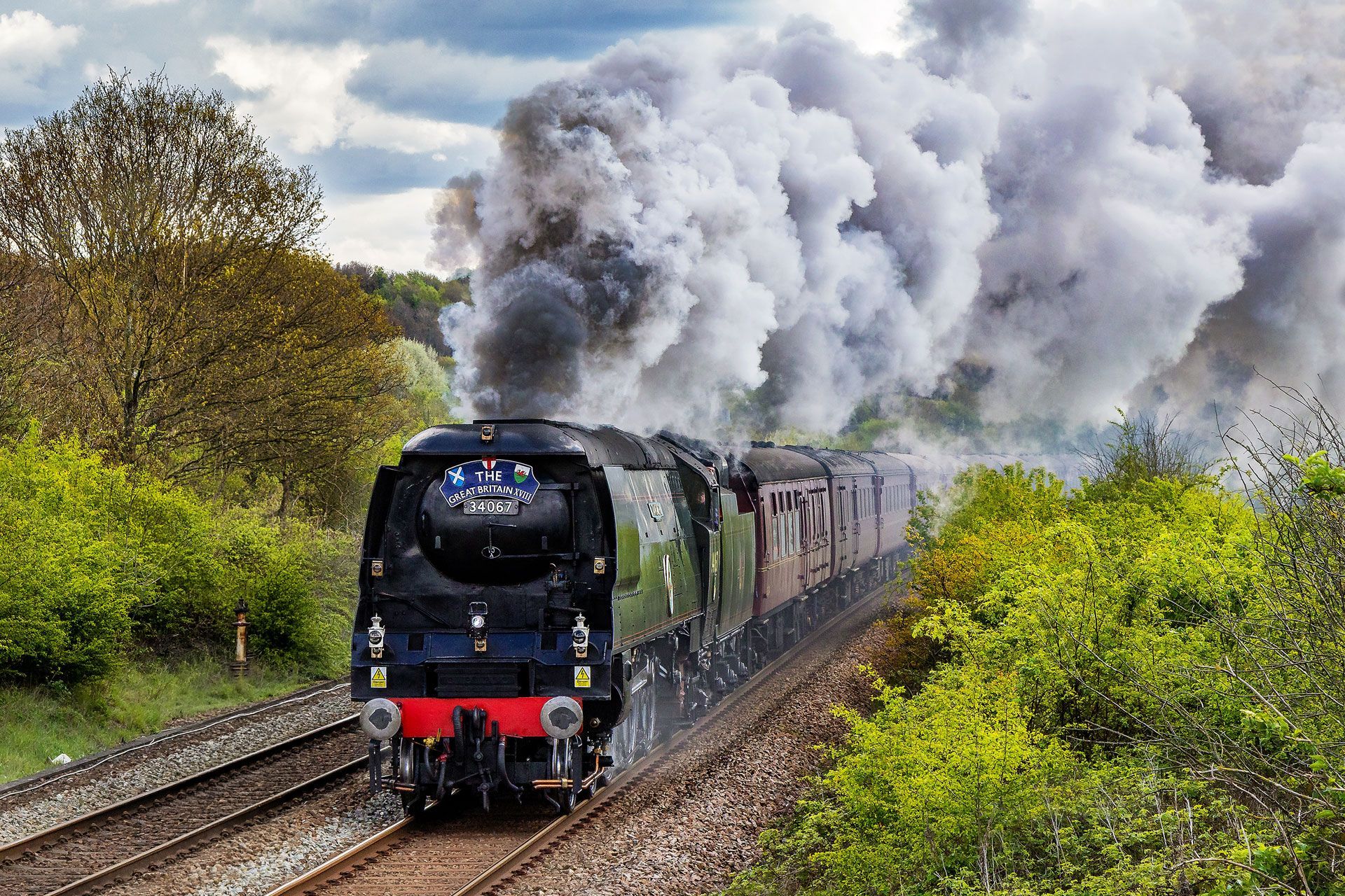 Steam locomotive racing through a green countryside, billowing thick white smoke
