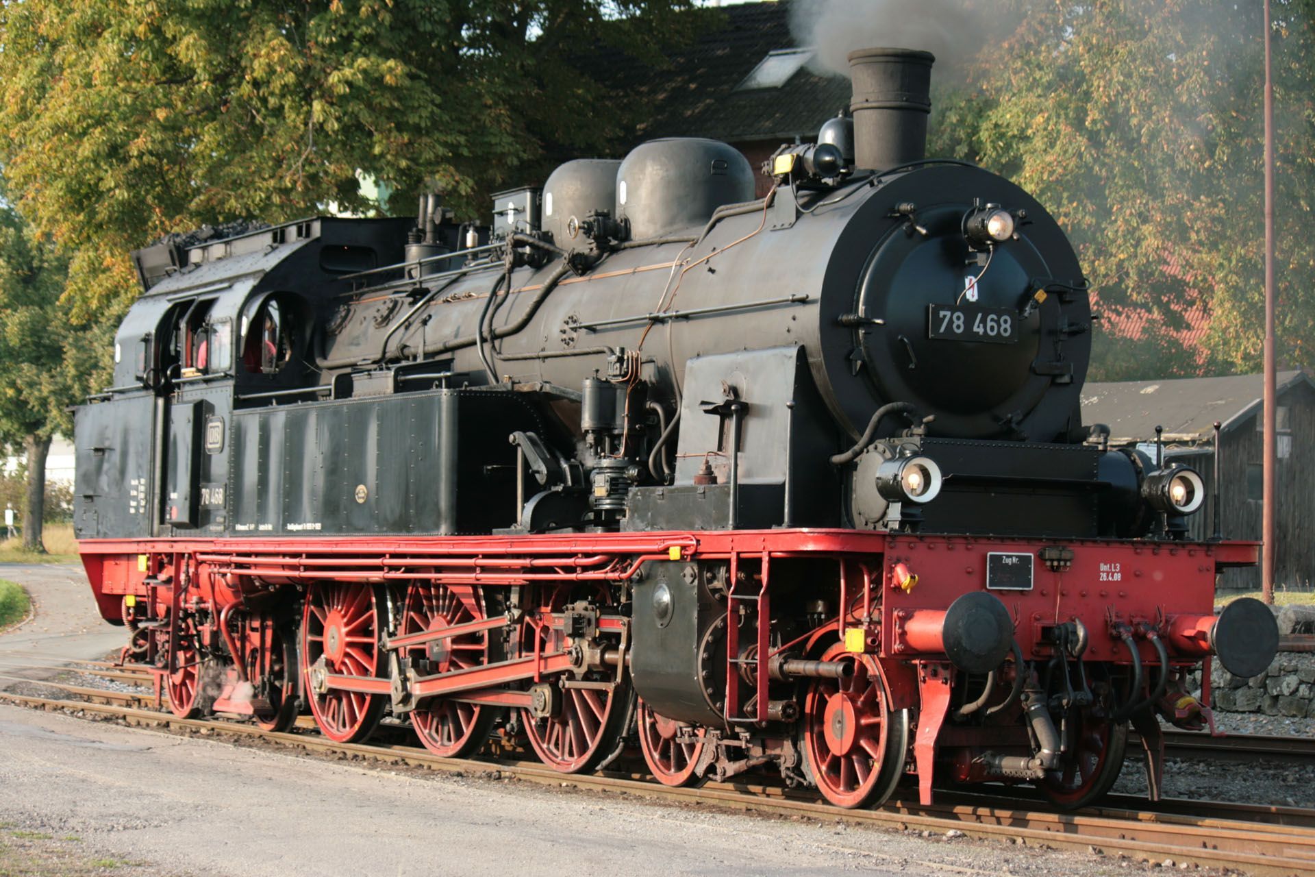 Black steam locomotive on tracks with red wheels, outdoors in daylight