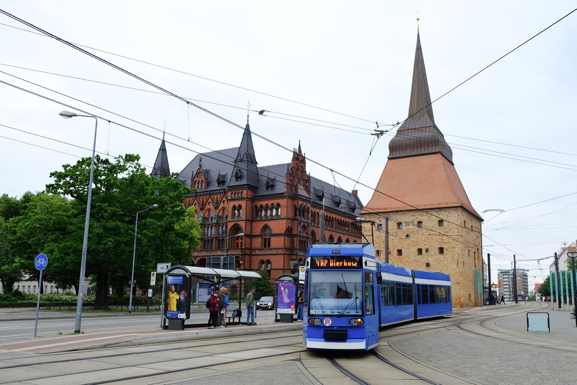 Tram and bus stop in front of historic brick buildings and a tall church tower on a city street