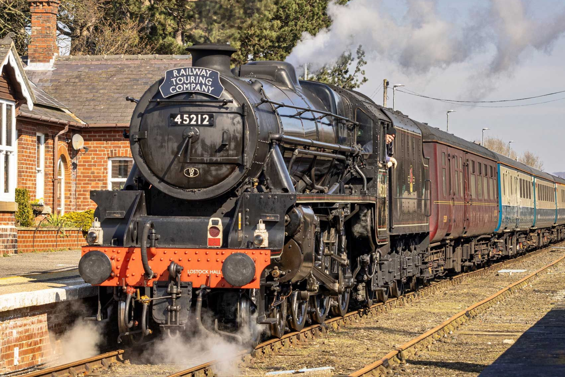 Black steam train at a station. Number 45212 on the front. Train is emitting steam and smoke.