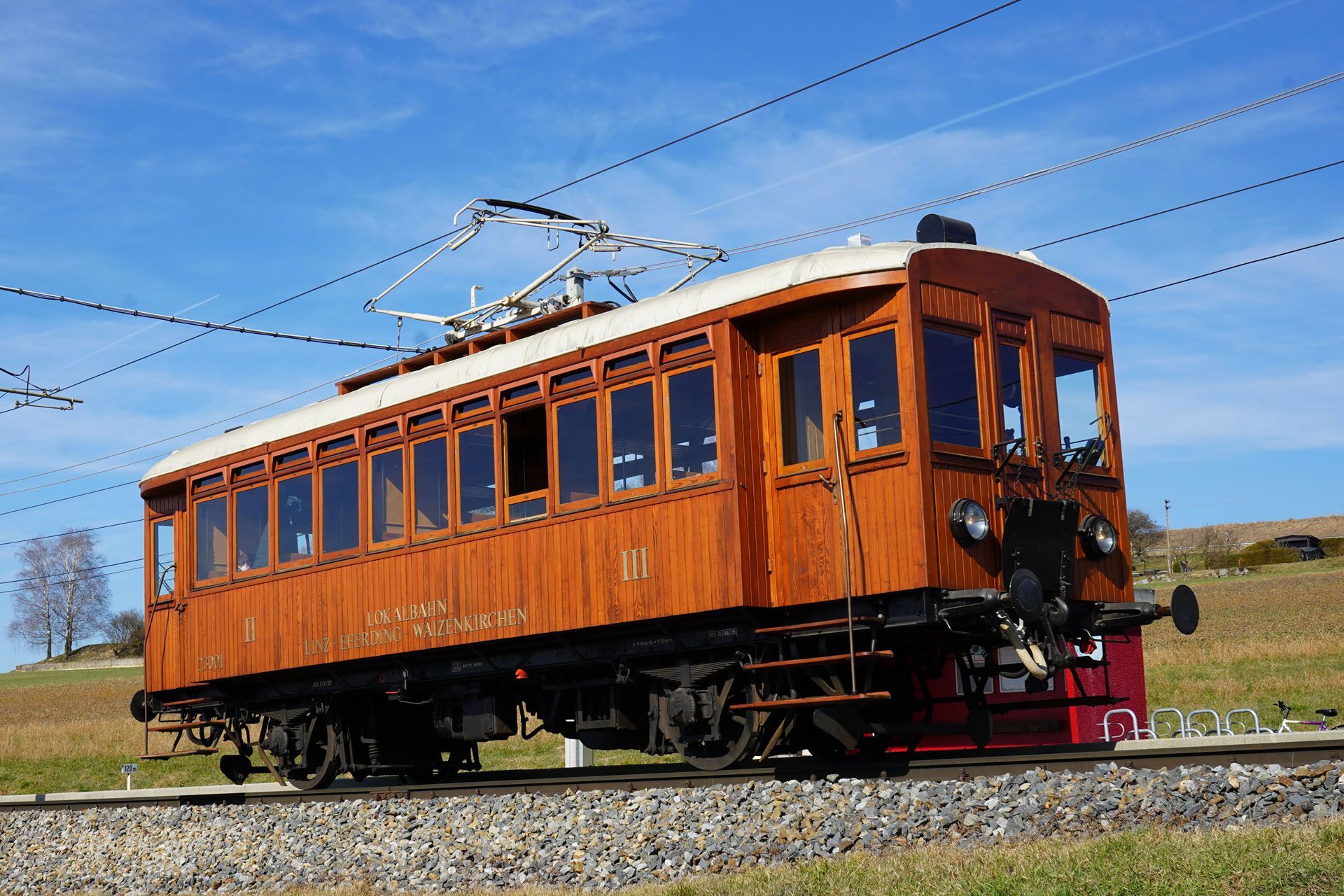 Wooden electric train car on tracks, under blue sky.