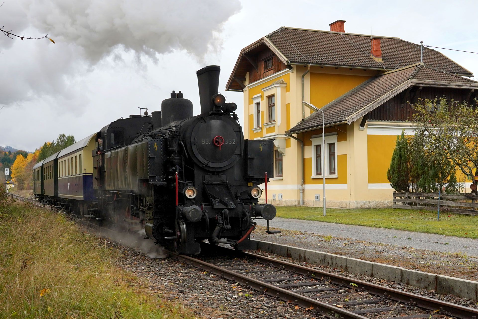 Steam train pulling into a yellow station, smoke billowing.