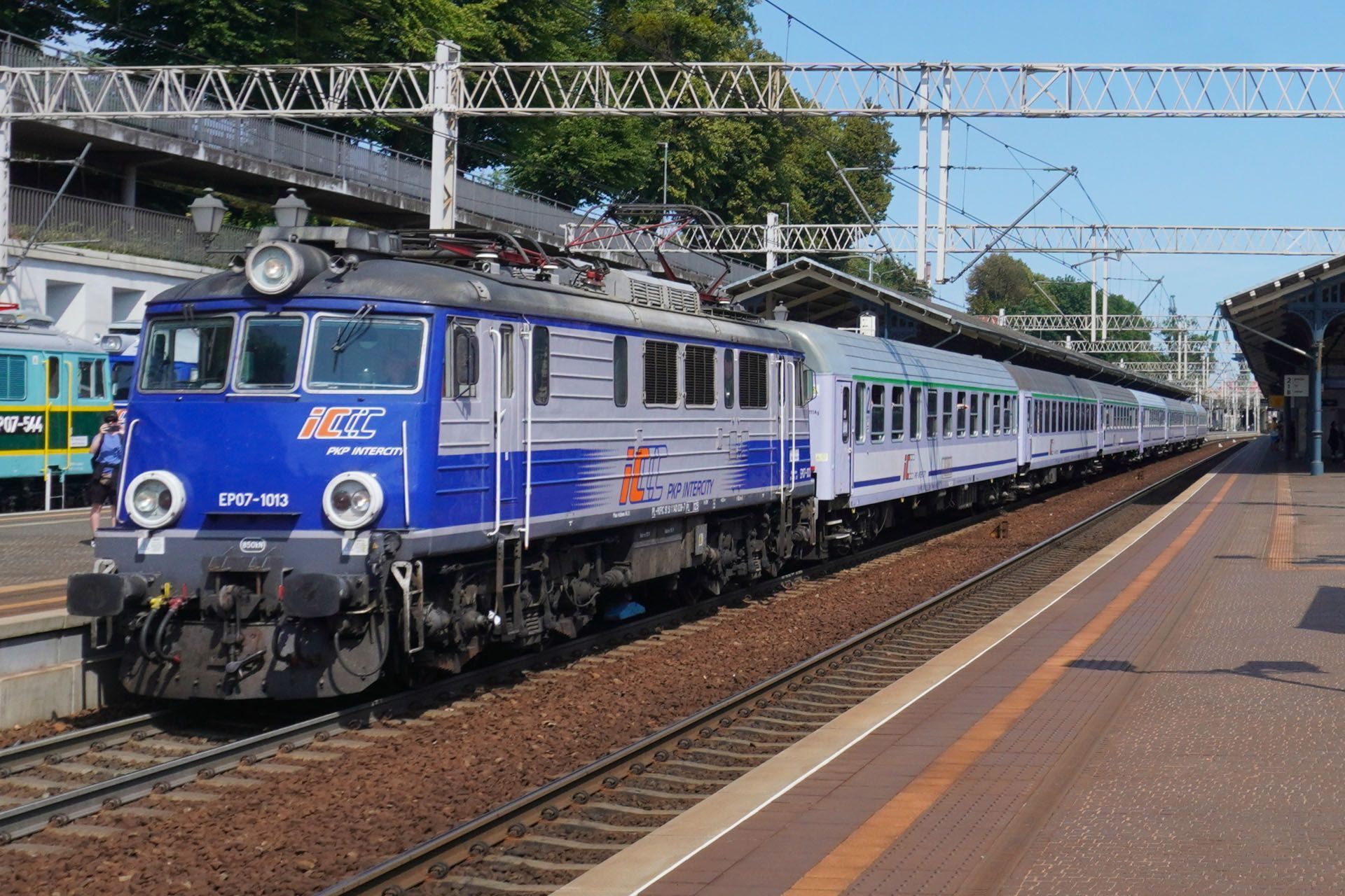 Blue and silver electric locomotive and passenger cars at a train station.