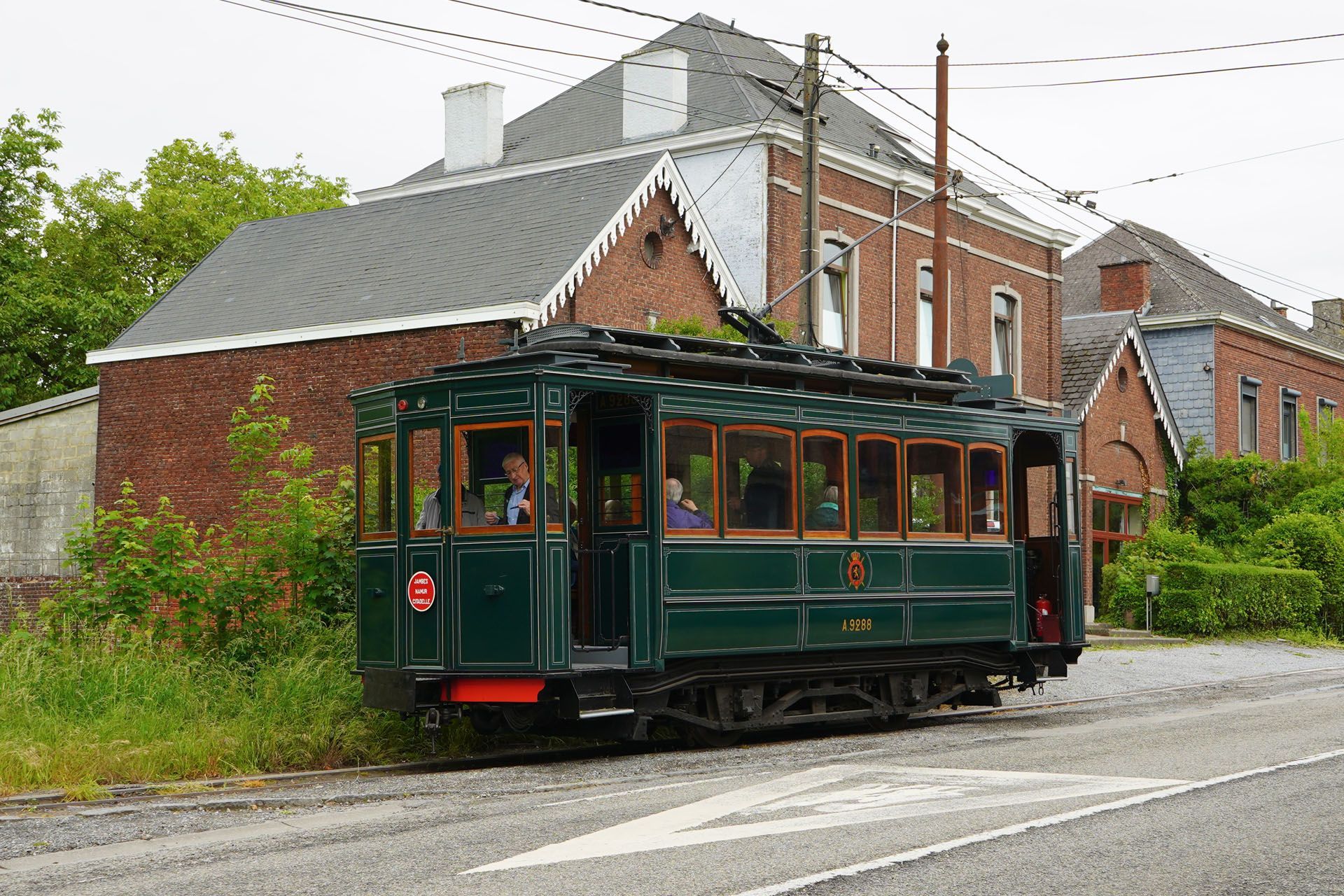 Green vintage trolley on tracks next to a brick building and road.