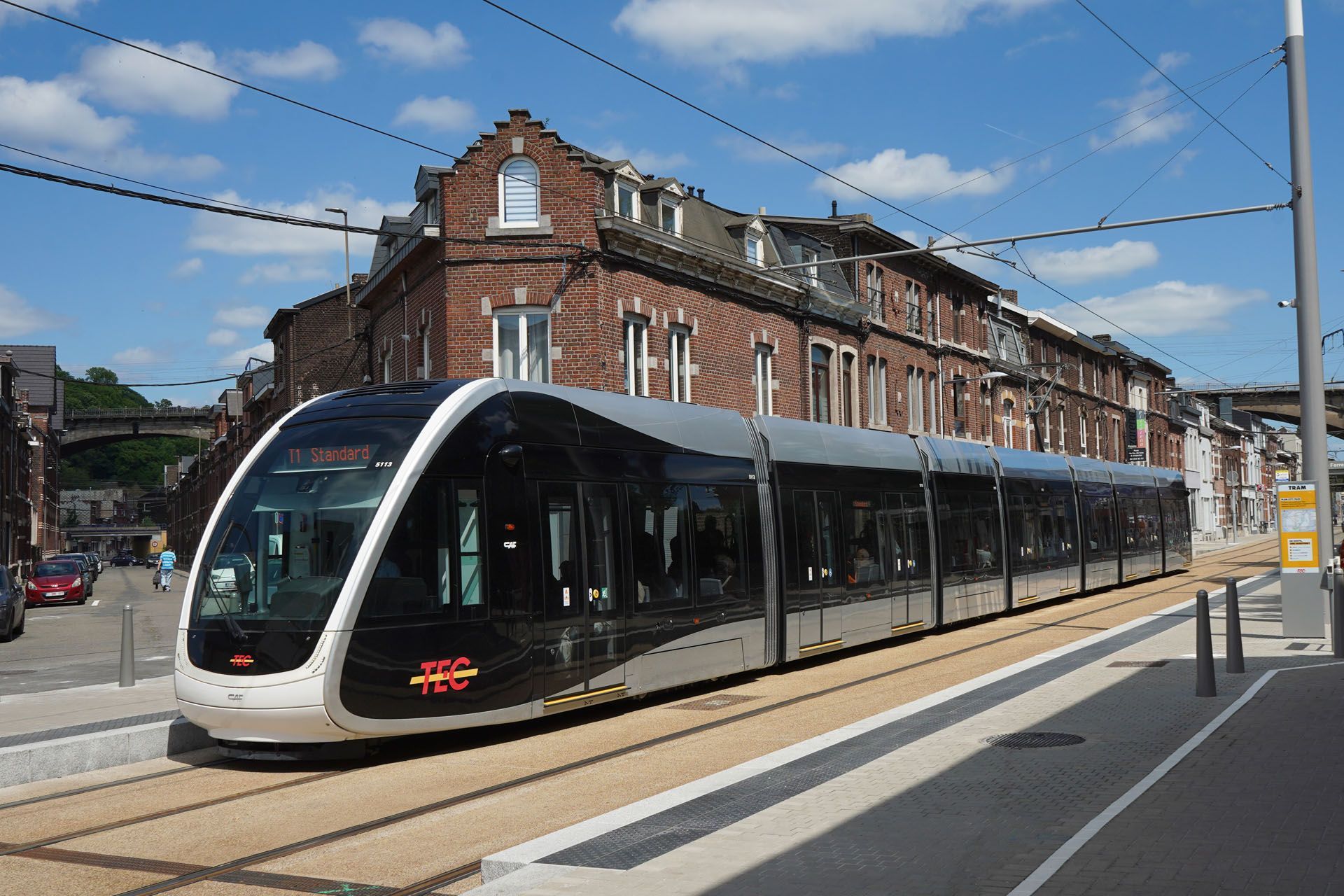 Tram on tracks next to a brick building. Bright day with a blue sky.