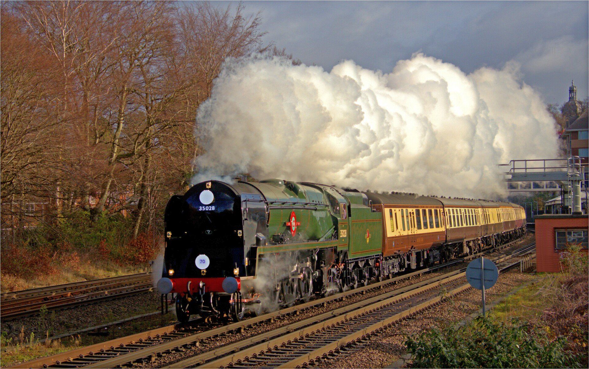 Steam train traveling on a track, emitting large plumes of white smoke against a clear blue sky.