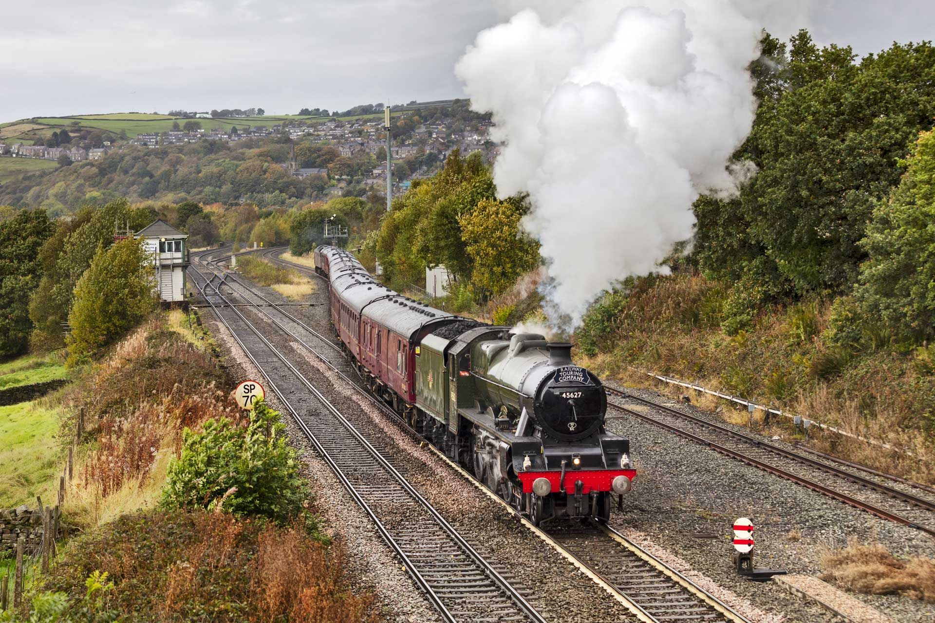 Steam train traveling on tracks through a green, hilly landscape.