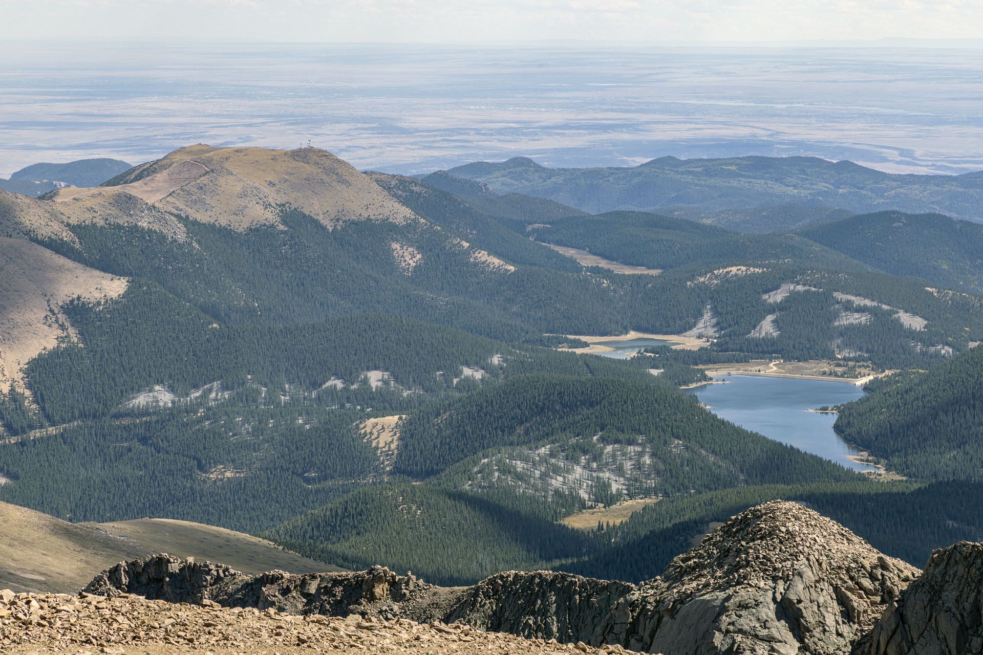 Mountain vista with dense evergreen forest, rocky peaks, and two lakes.