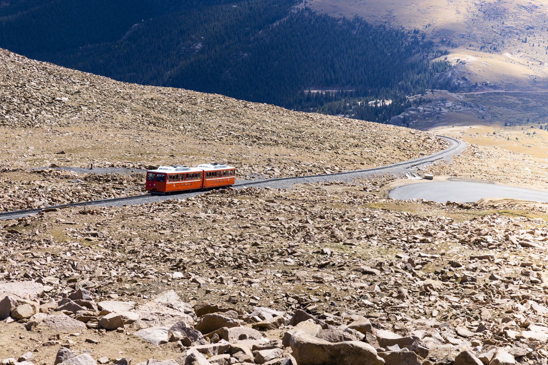 Orange cogwheel train travels on a winding road up a rocky mountain.