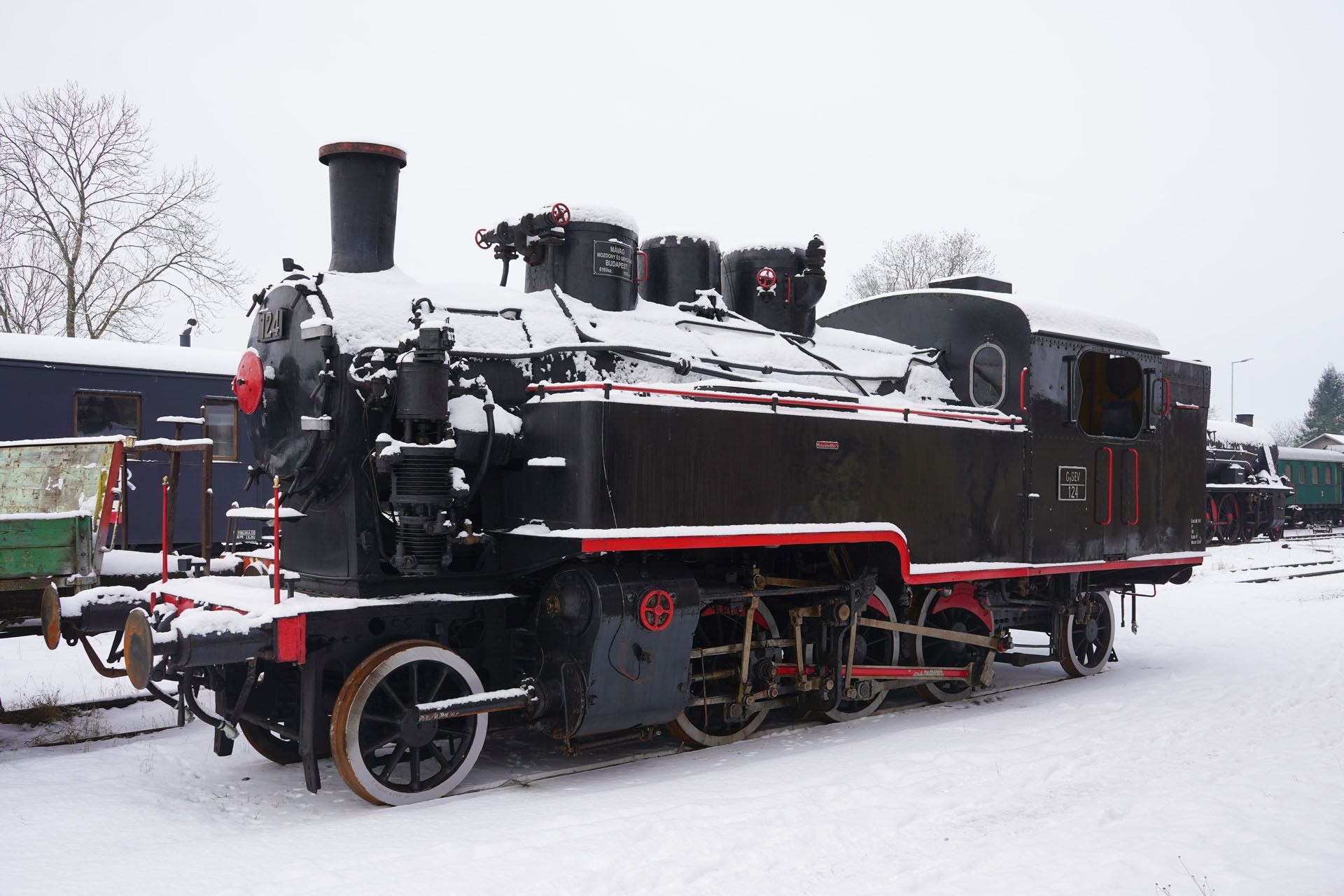 A black steam locomotive with red accents sits in a snowy yard during winter.
