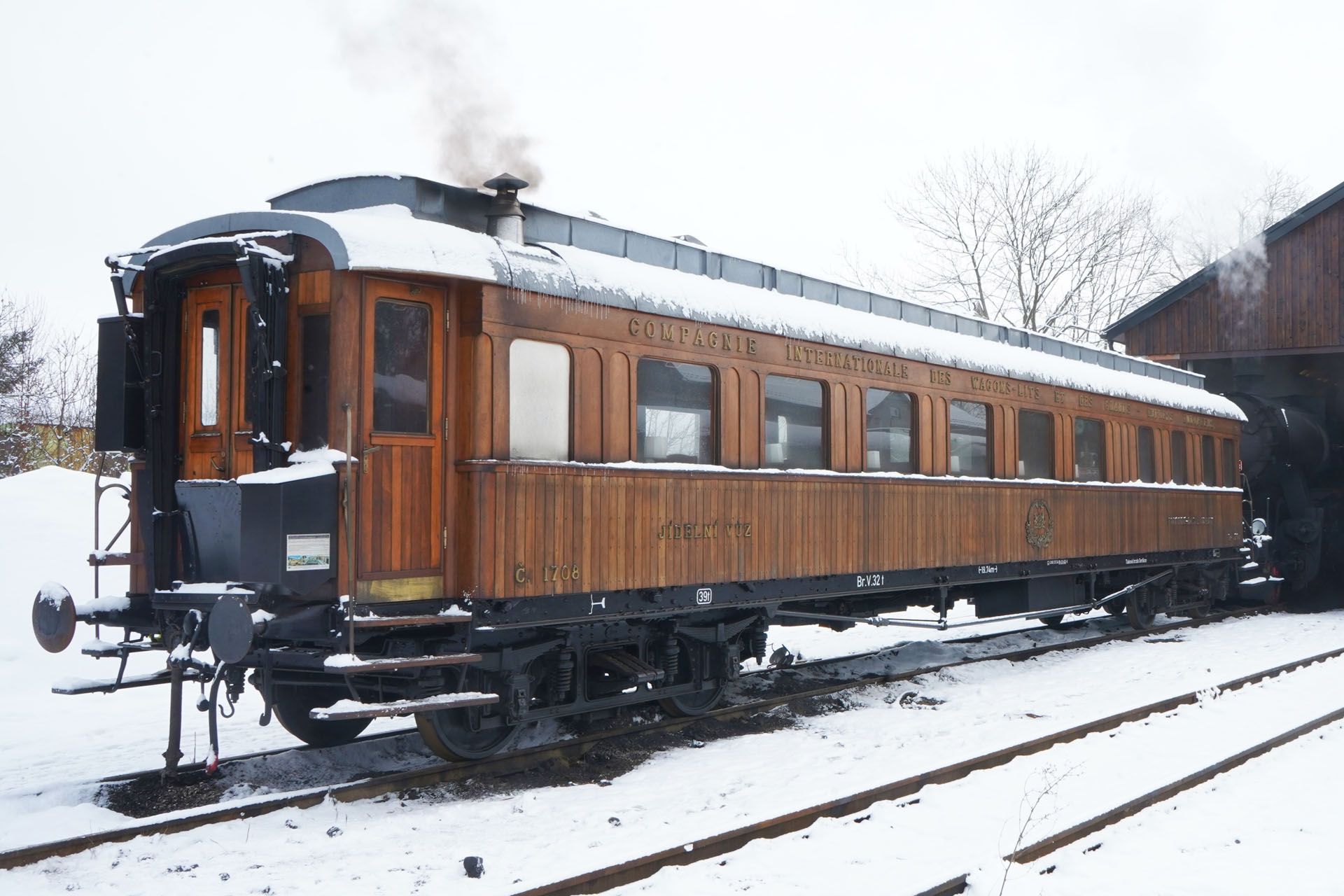An old-fashioned wooden passenger train car sitting on tracks covered in snow.