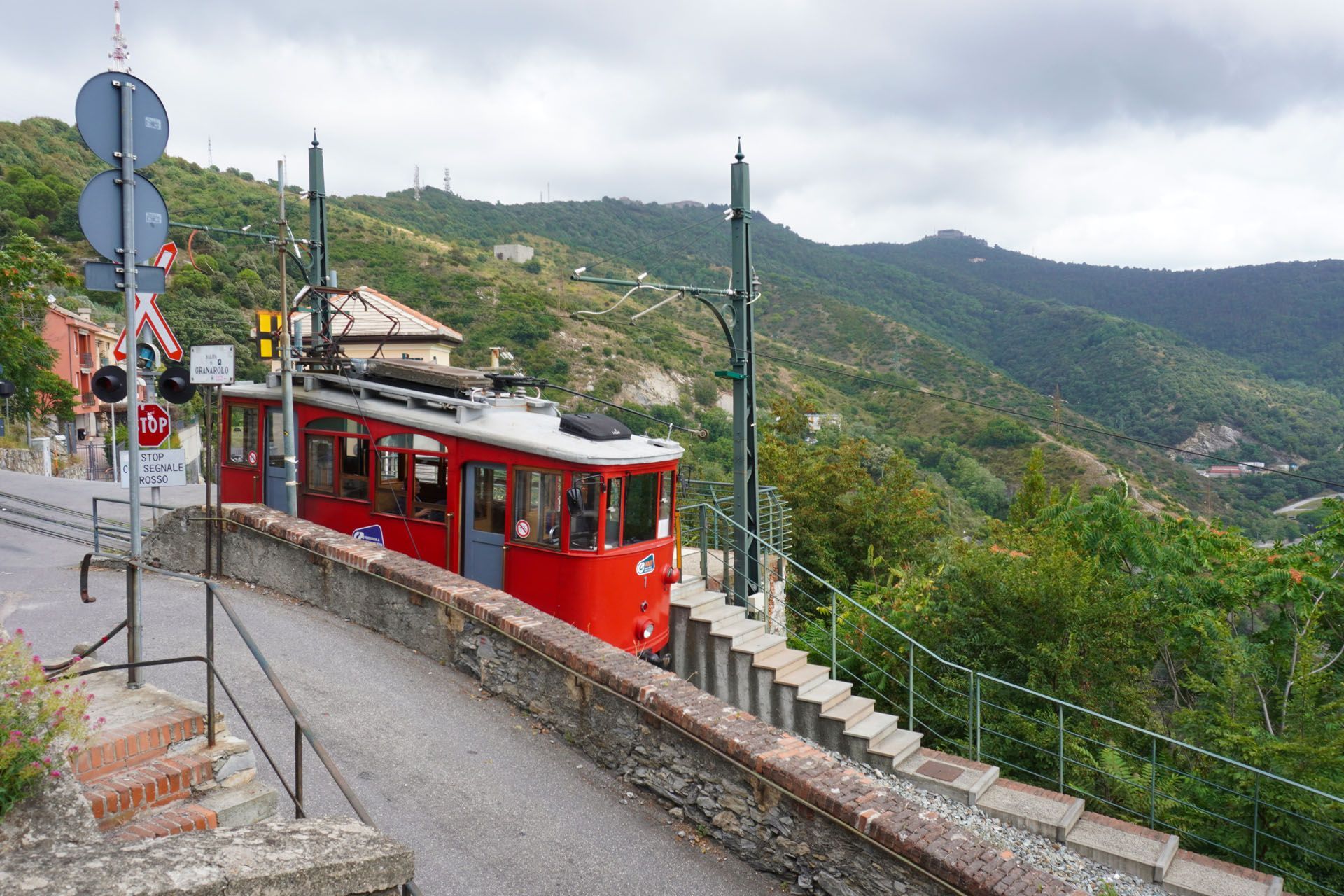Red funicular train ascending a steep hill with green, mountainous landscape in the background.