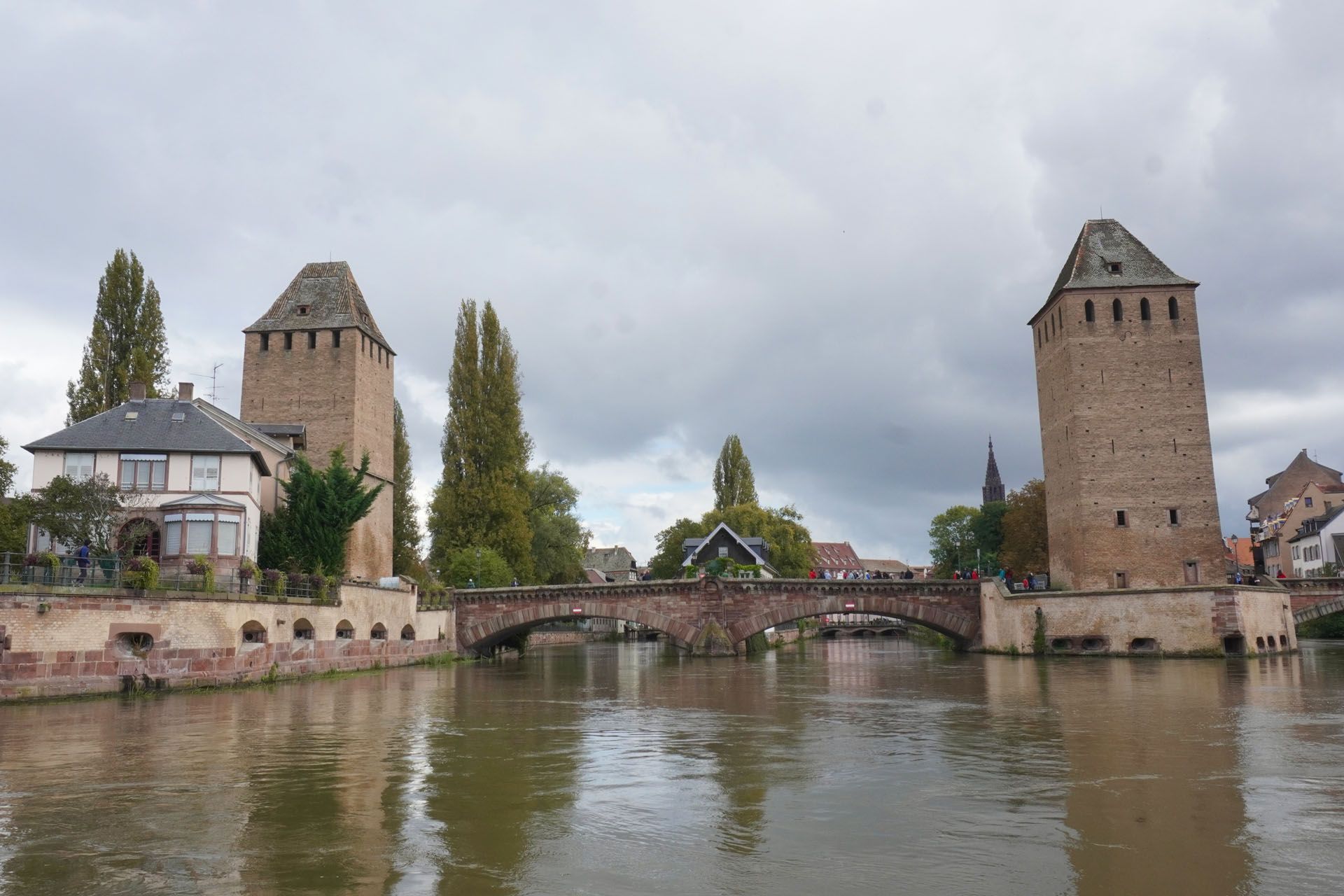 Stone towers and bridge over a canal in Strasbourg, France, under an overcast sky.