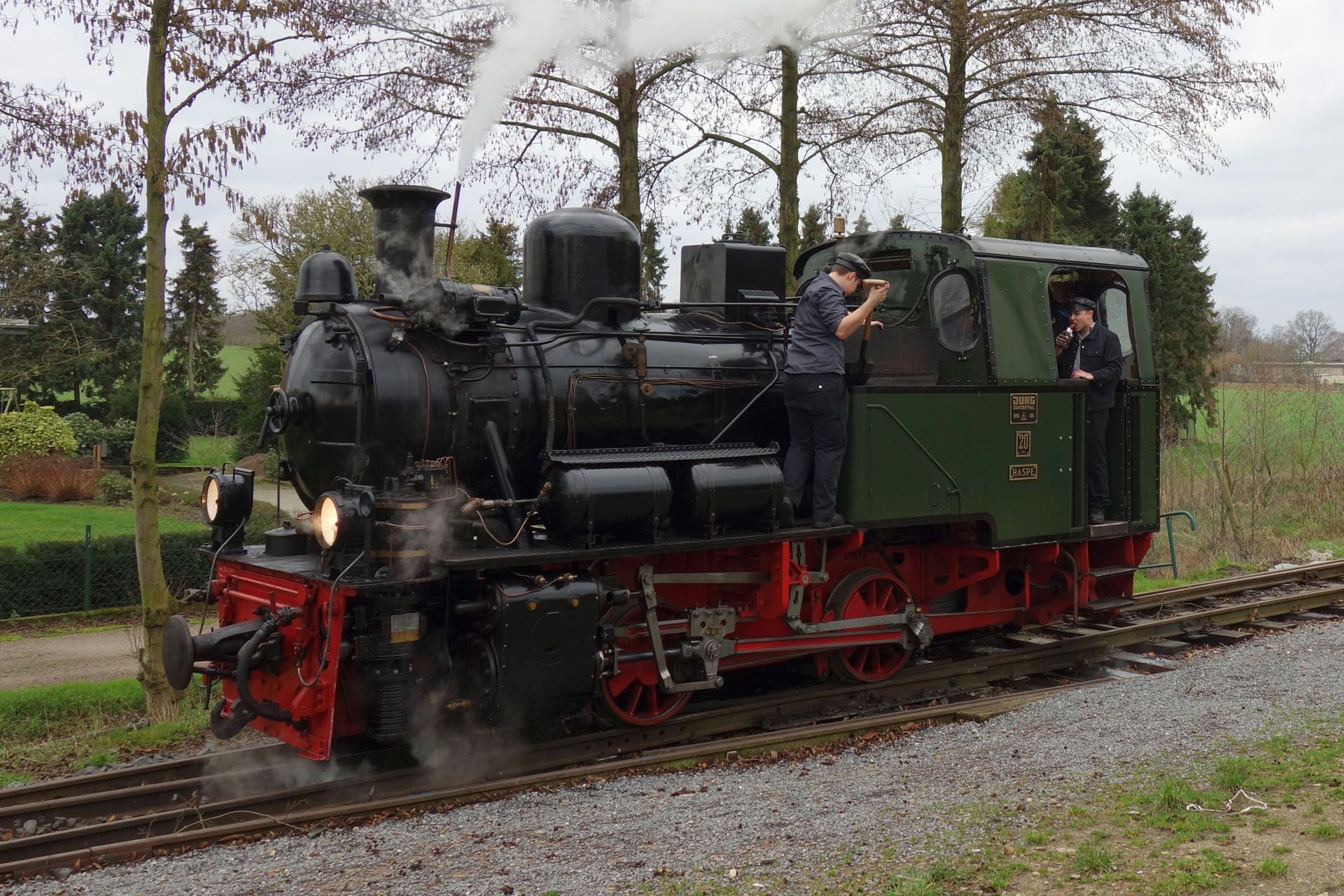 Black steam locomotive on tracks with crew members.