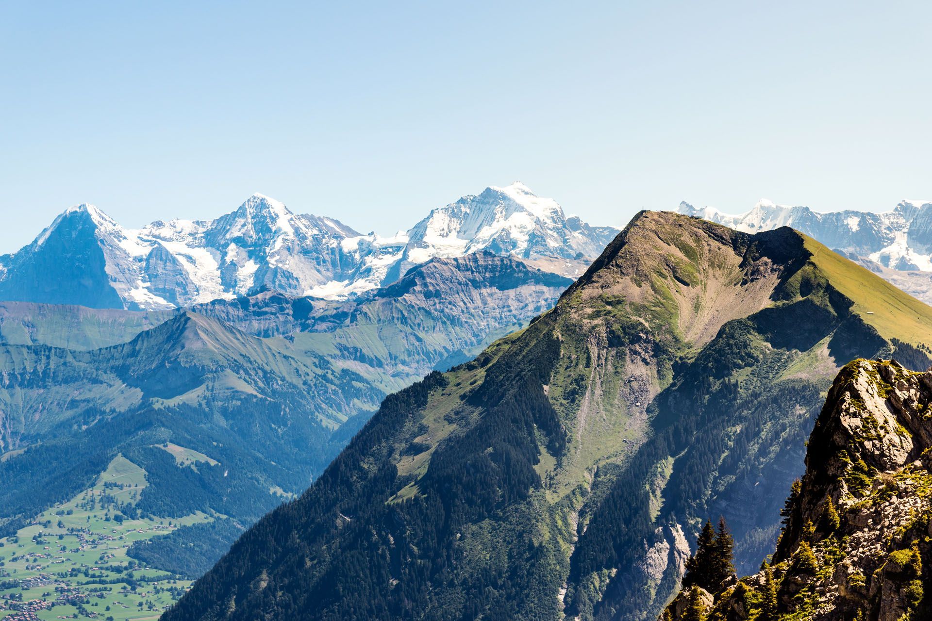 Mountains with snow-capped peaks under a clear blue sky. Lush green slopes in the foreground.