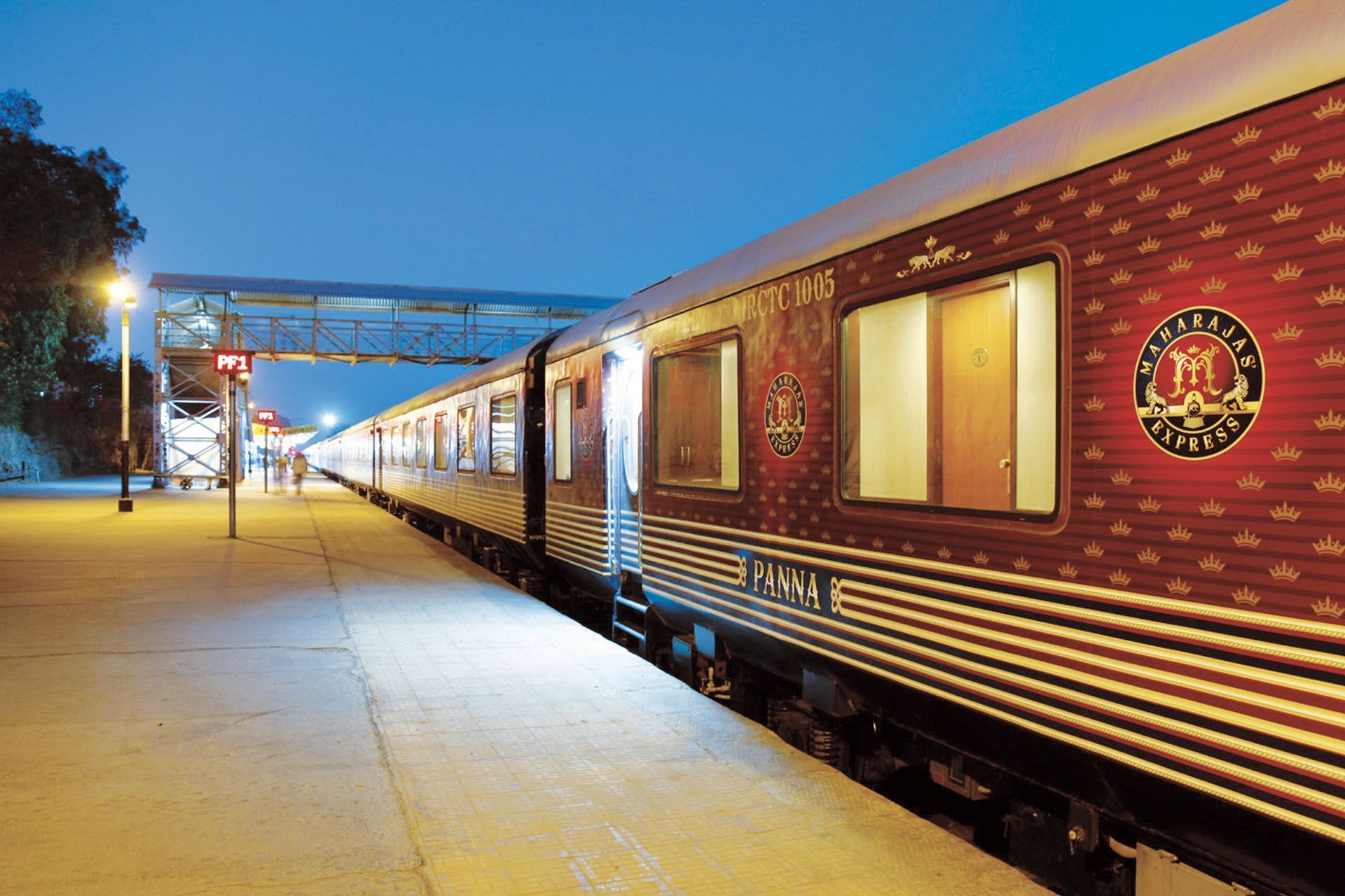 Maroon passenger train at a station platform at dusk, with lit windows and a snowy ground.