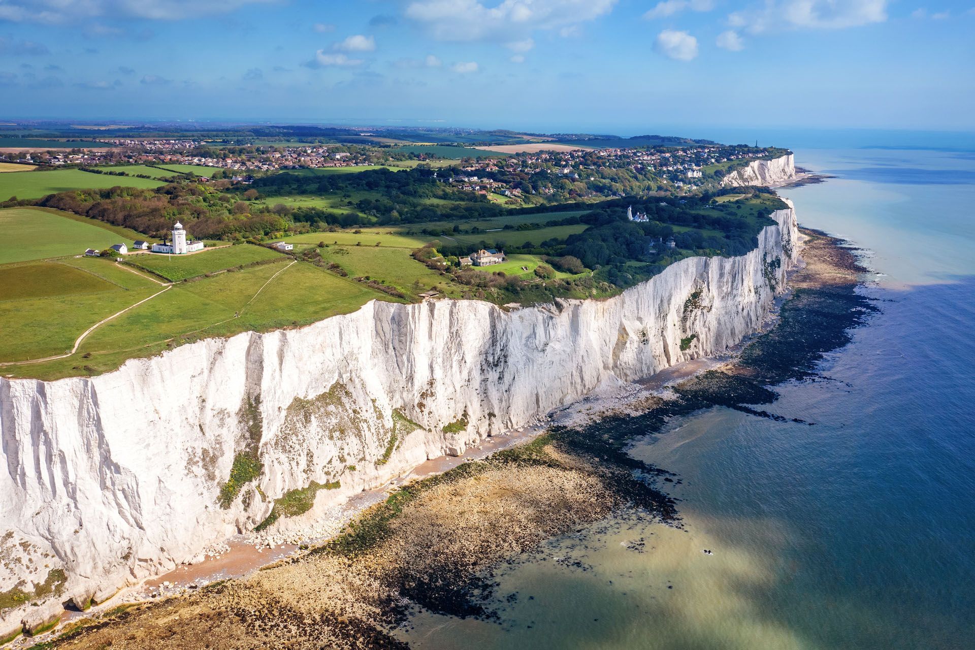 White Cliffs of Dover meeting the English Channel, with green fields and a town on the horizon.