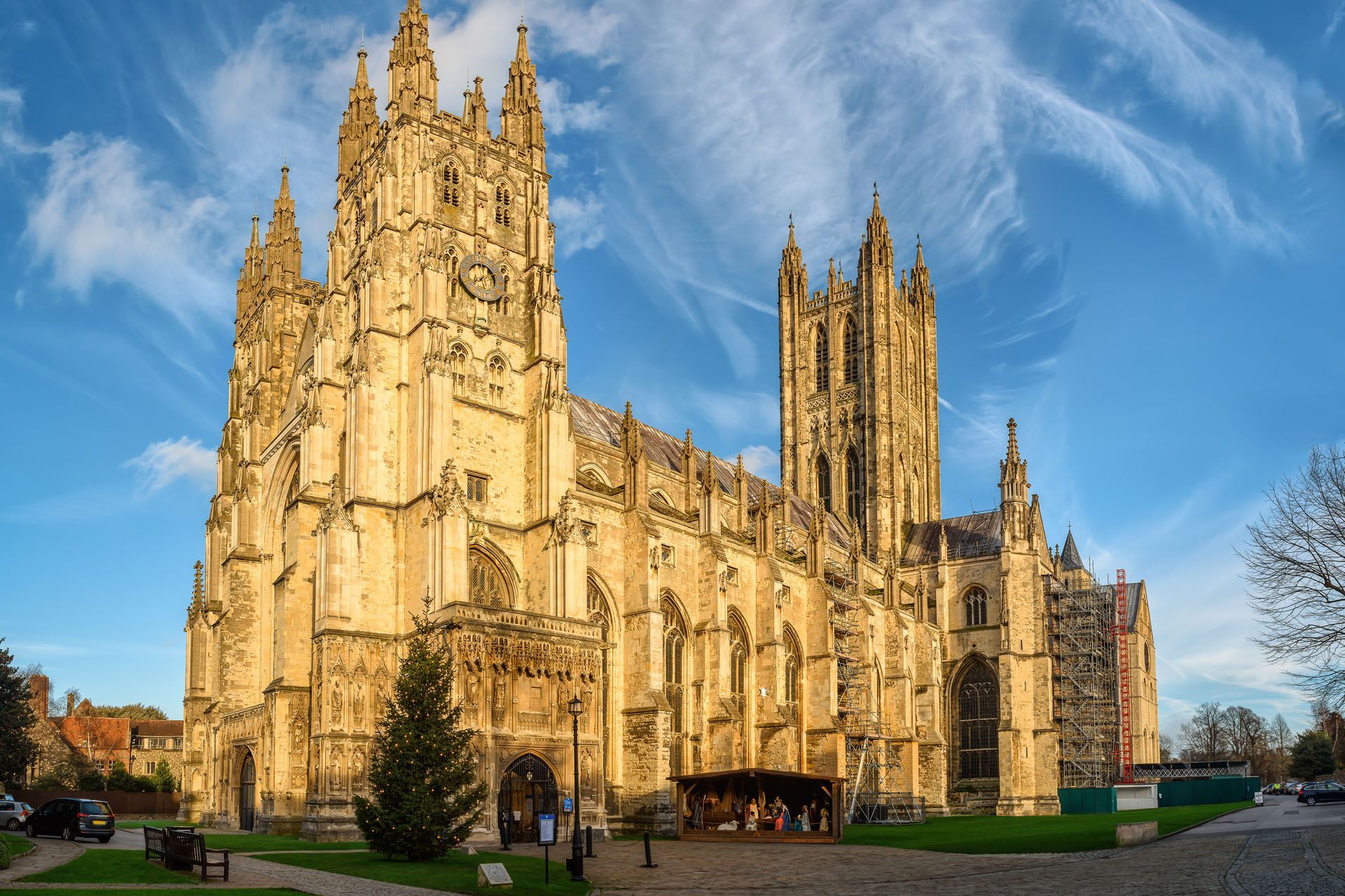 Canterbury Cathedral, a large stone structure with towers, under a bright blue sky with wispy clouds.