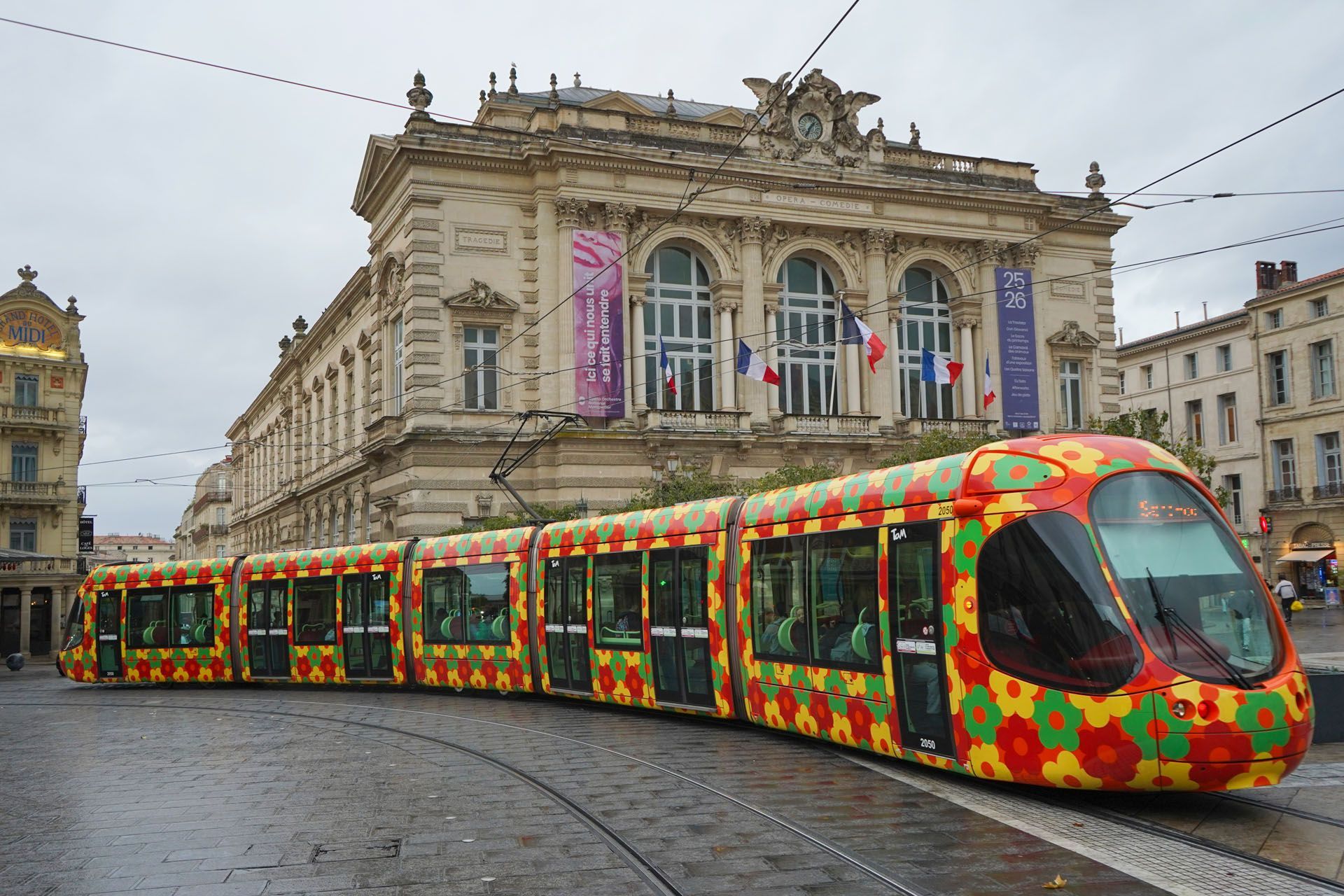 Colorful tram on tracks in front of a classical building with French flags and banners.
