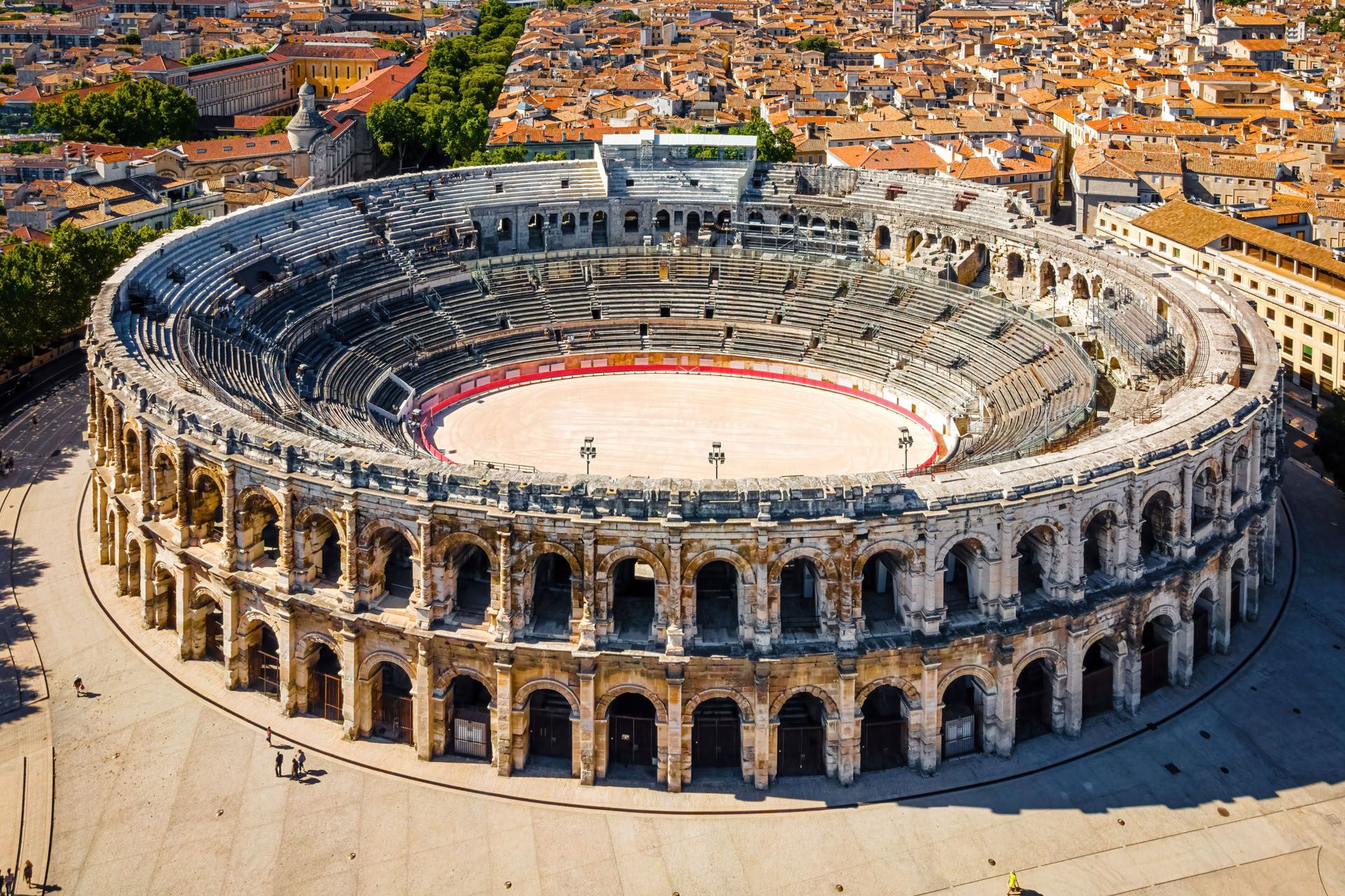 An aerial view of the Roman amphitheater in Nîmes, France; gray stone structure with an elliptical arena.