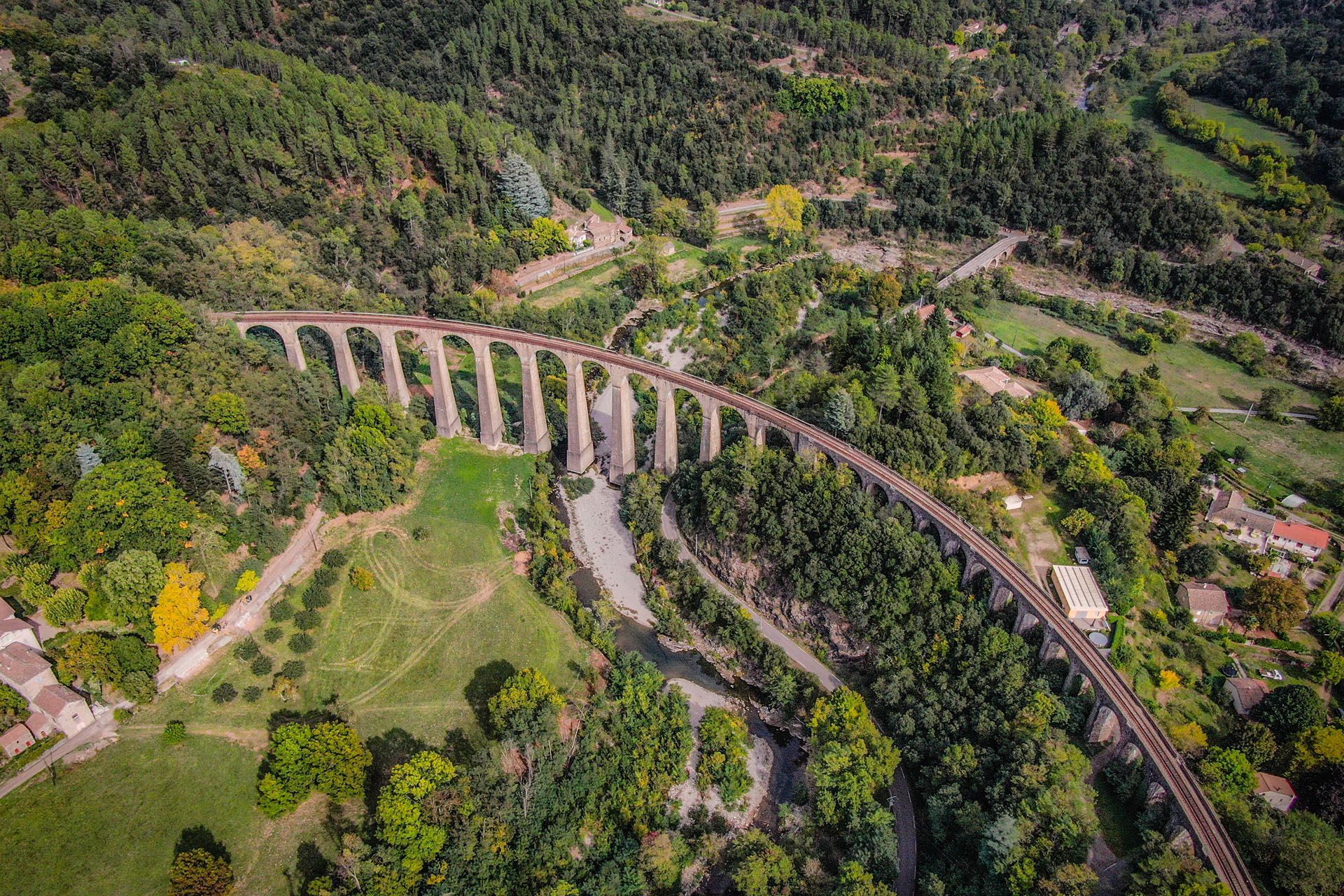 Stone railway viaduct arched over a river valley, surrounded by green trees and buildings.