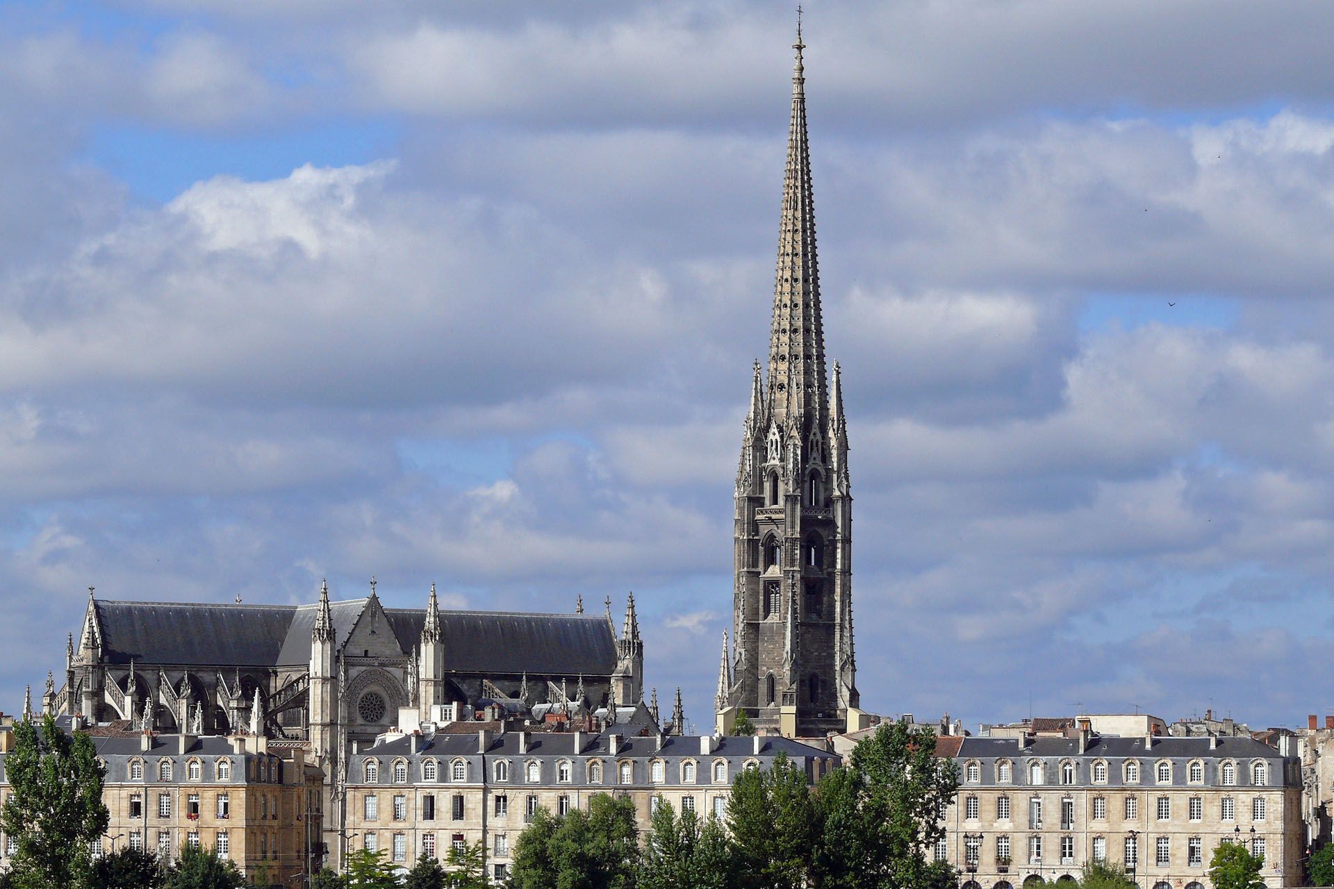 View of Bordeaux Cathedral and a tall, ornate bell tower against a cloudy sky.