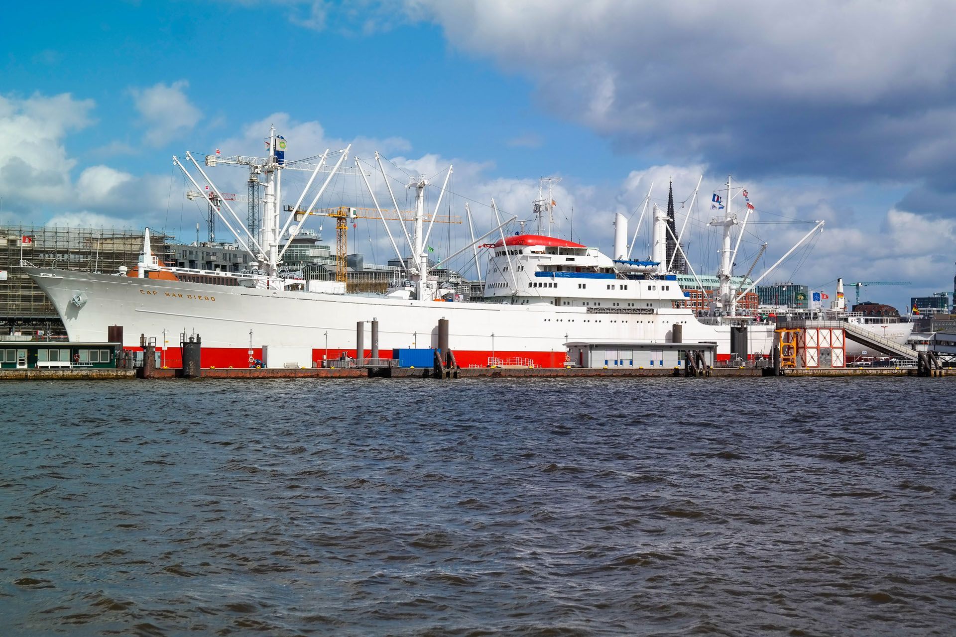 Large white and red ship docked at a harbor on a cloudy day.