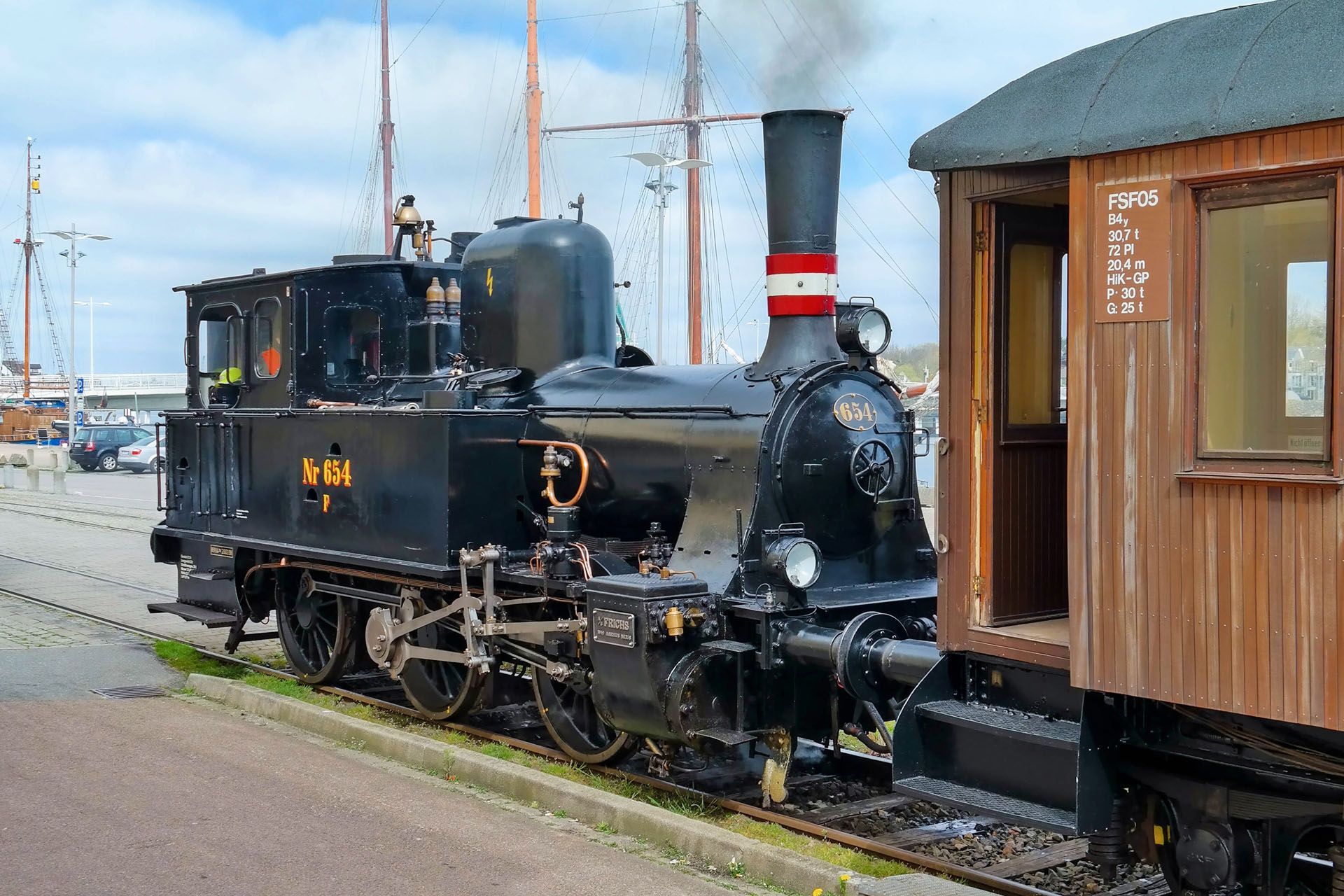 Black steam locomotive with red and white striped smokestack next to a wooden train car.