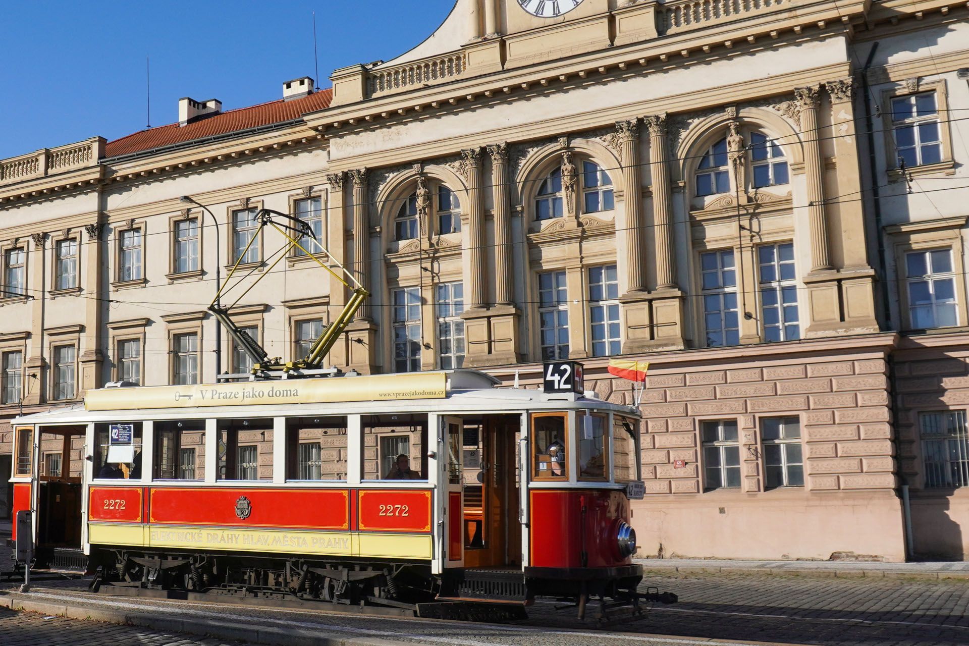 Red and white tram car in front of a large, ornate building.
