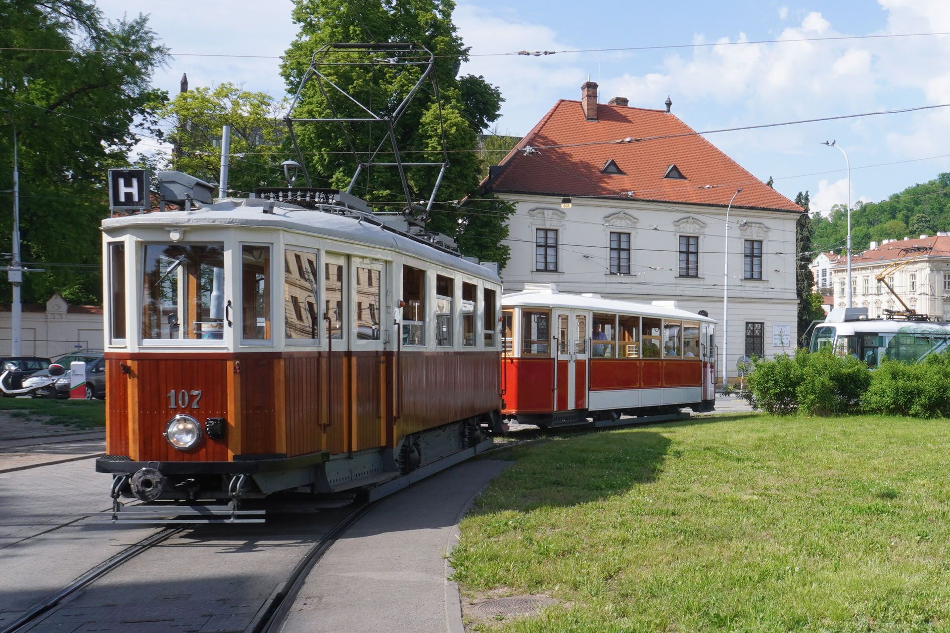Two vintage red and cream trams on tracks in front of a white building with a red tile roof.