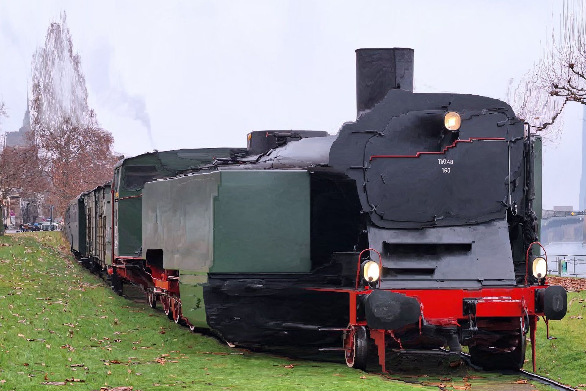 Black steam locomotive with red trim on tracks in a grassy outdoor setting