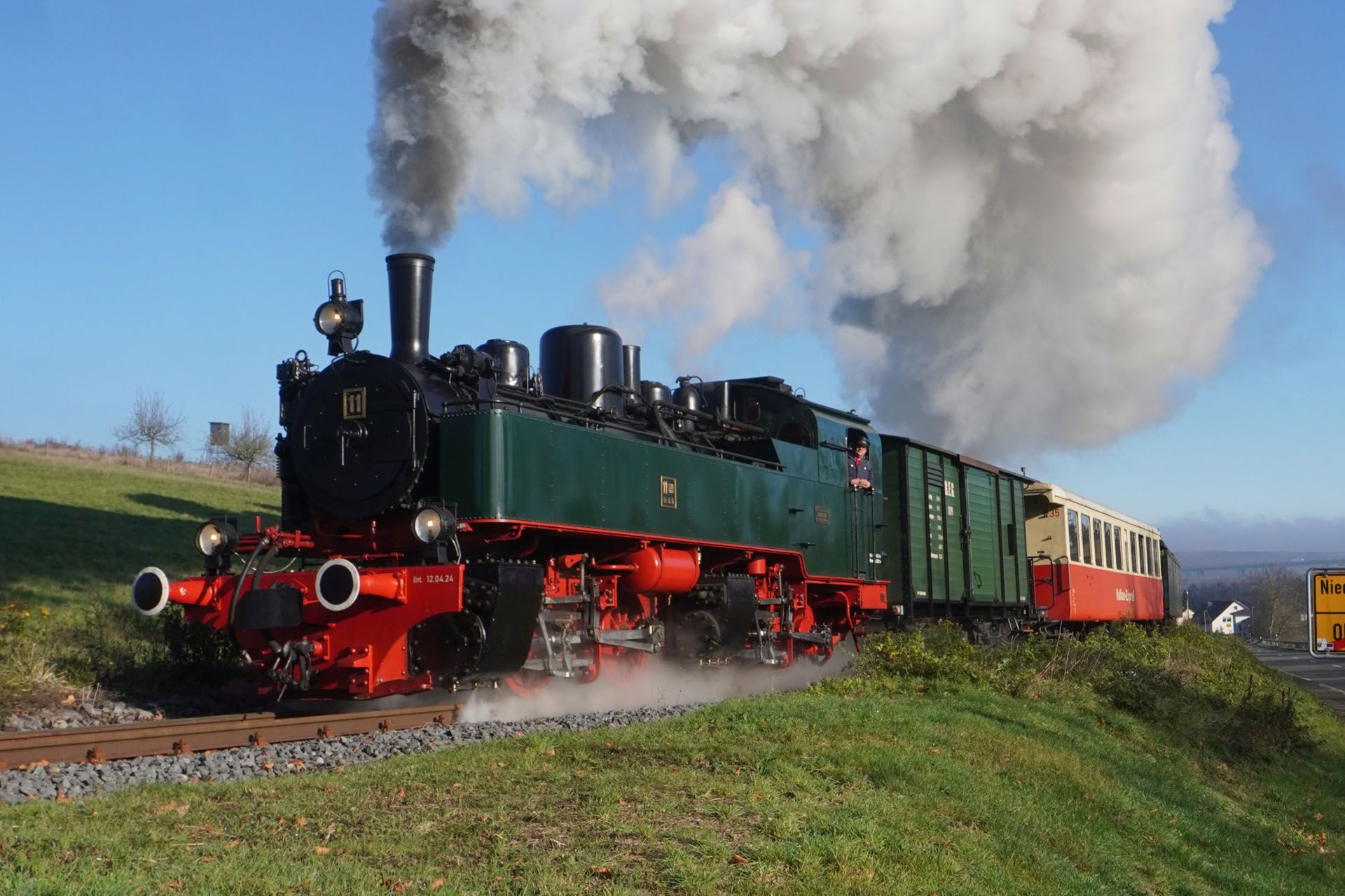 Steam locomotive pulling green freight cars through a grassy countryside, billowing smoke