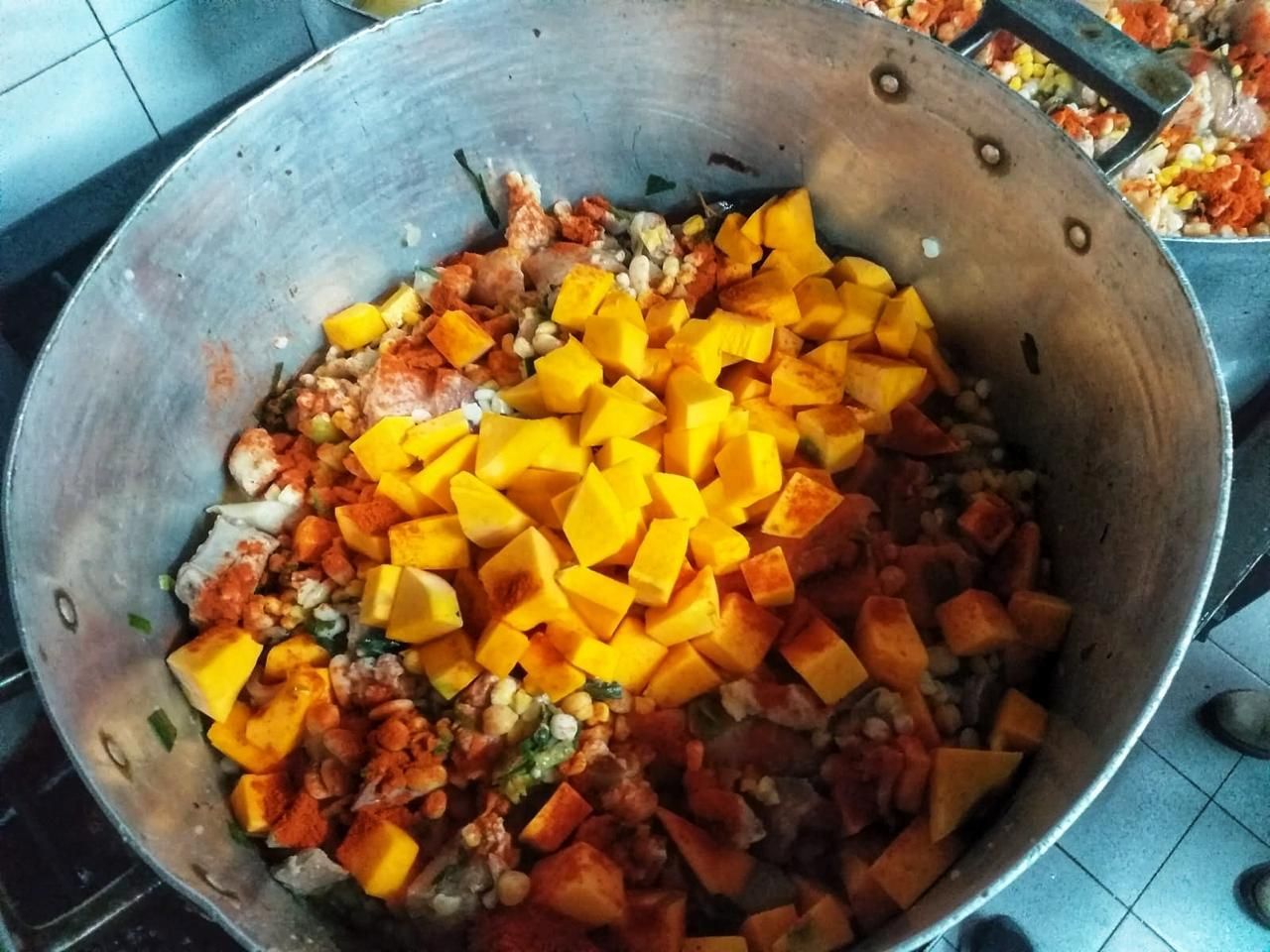 Olla grande de metal llena de calabaza amarilla picada y varios condimentos, lista para cocinar en la cocina.