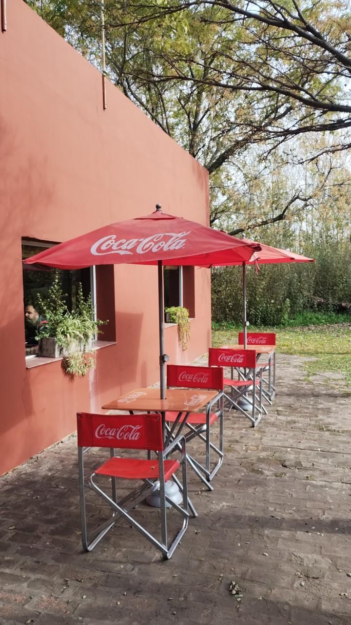 Tres mesas y sillas de café rojas con la marca Coca-Cola, acompañadas de sombrillas a juego