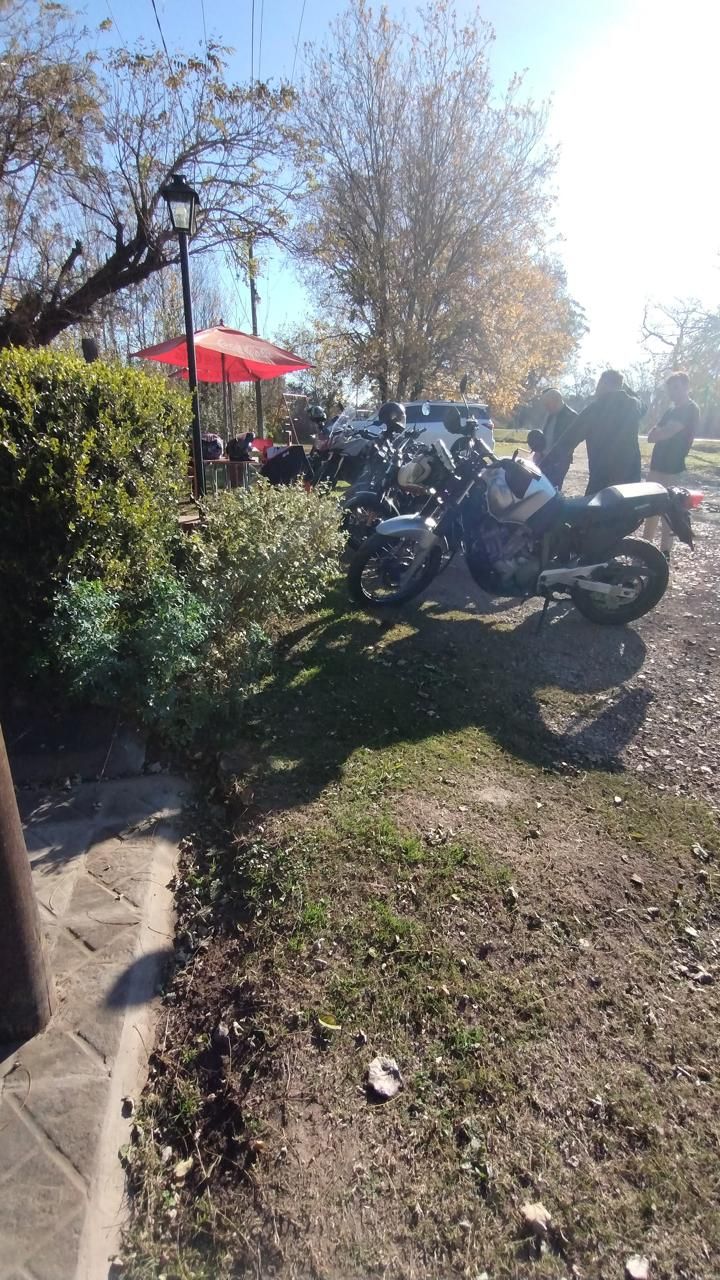 Una motocicleta estacionada en un tramo de grava cerca de un seto verde y una sombrilla roja de exterior en un día soleado.