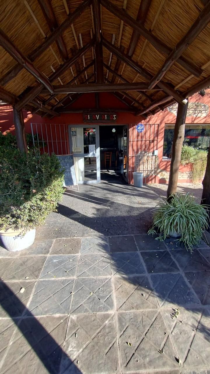 La entrada de piedra a un edificio con techo de paja, que cuenta con una puerta de cristal y dos grandes macetas con plantas.