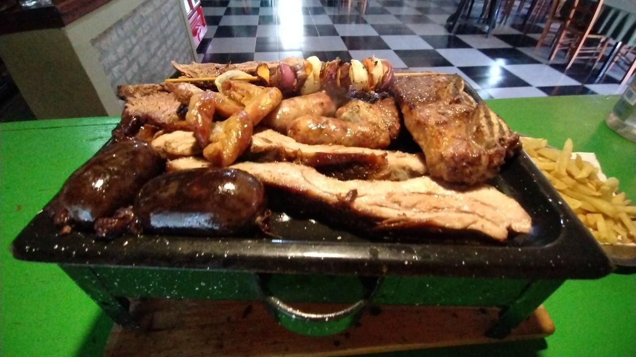 Una parrillada variada servida en una plancha de mesa, que incluye salchichas, filetes 