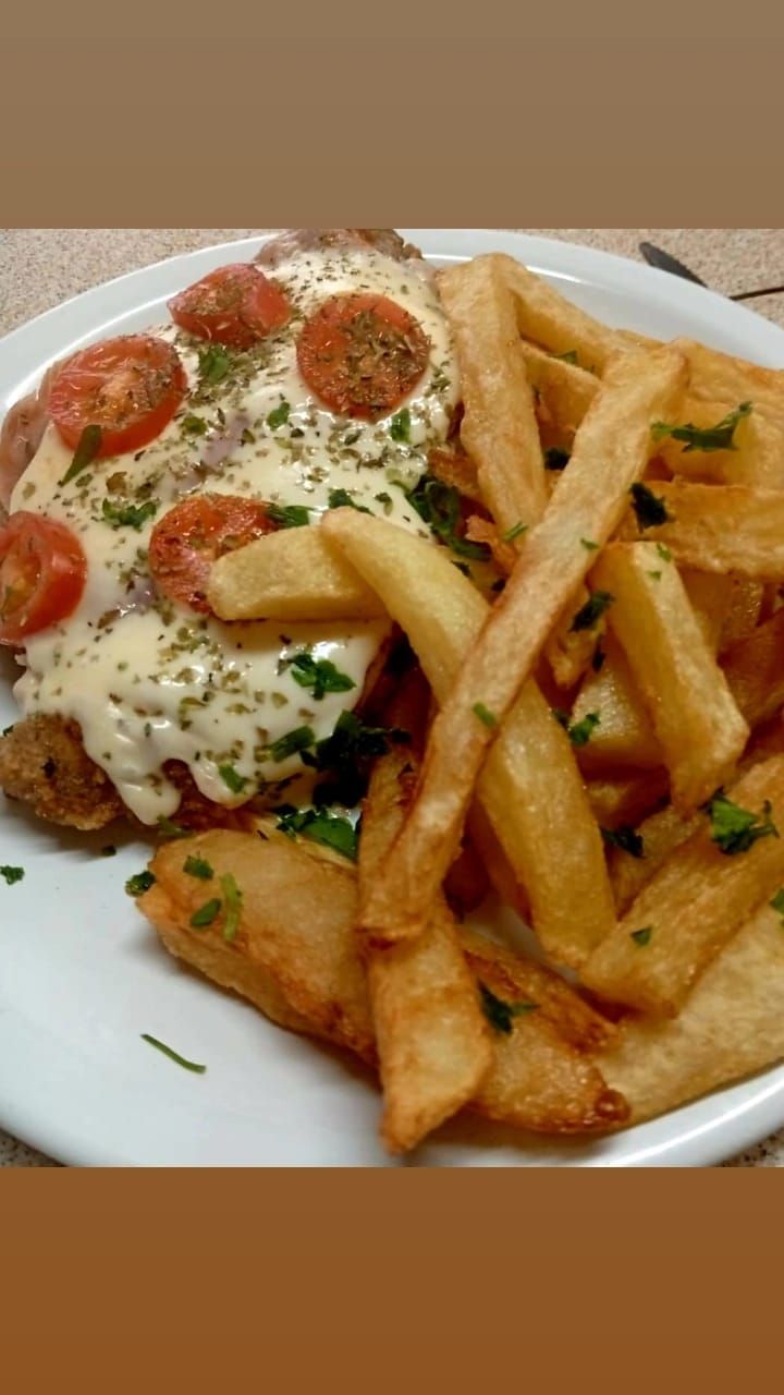 Un plato que incluye pollo empanizado cubierto con queso fundido, tomates cherry y hierbas, servido con papas fritas doradas.