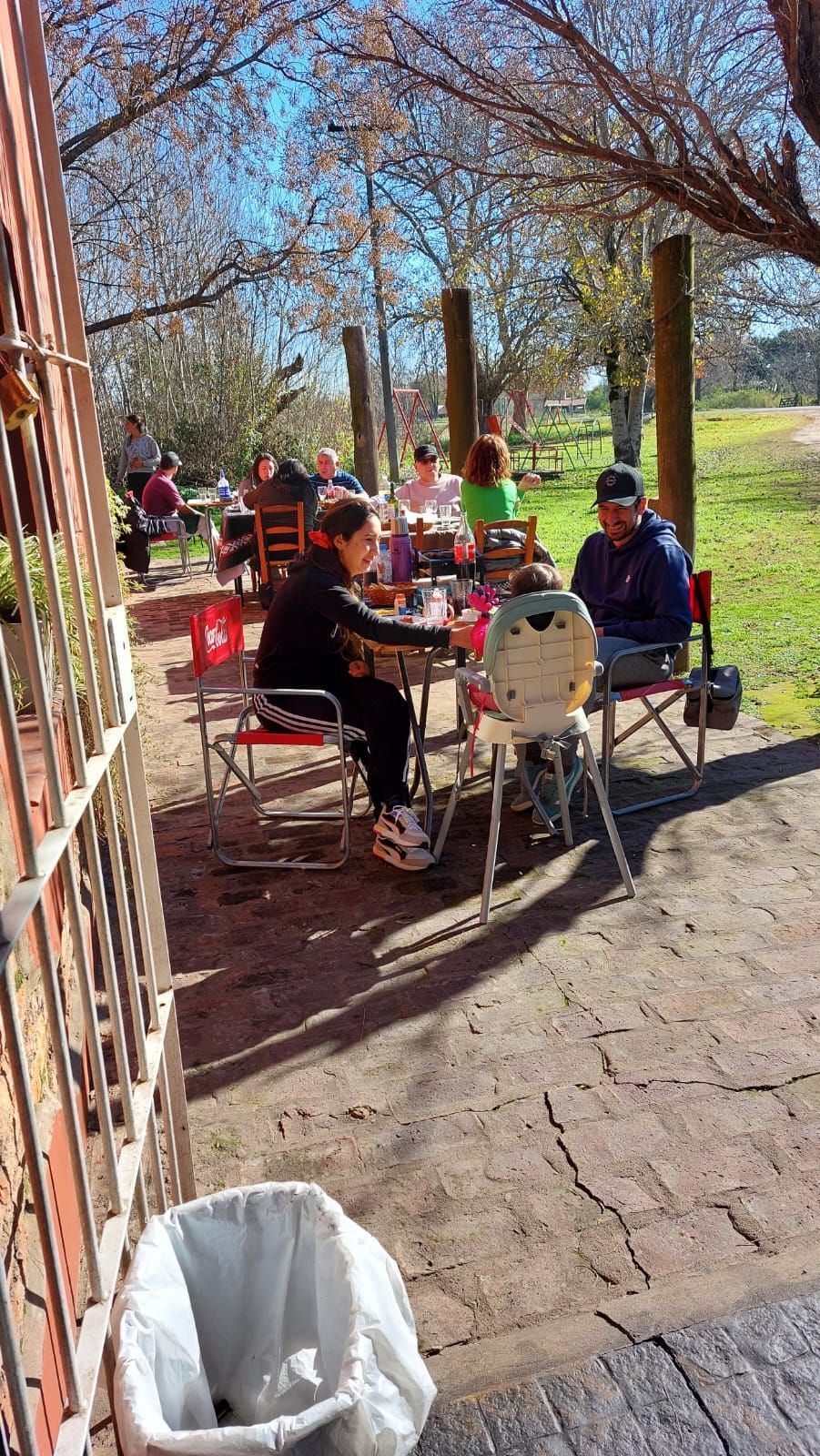 Gente comiendo al aire libre en un día soleado en una terraza de un café a la sombra de árboles en flor.