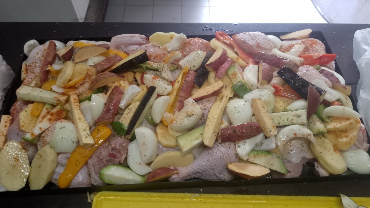 Una bandeja para hornear llena de muslos de pollo crudos, patatas en rodajas