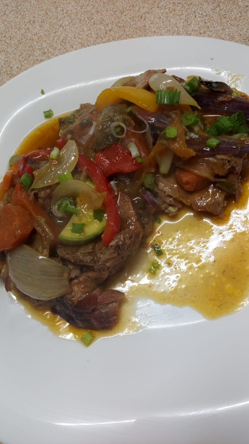 Un plato de carne sellada cubierta con una mezcla salteada de pimientos, cebollas, calabacines 