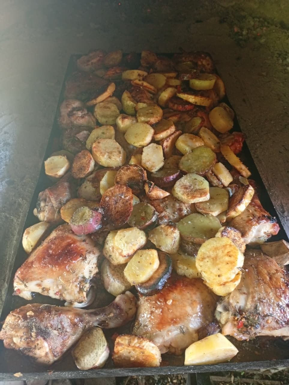 Una bandeja de horno grande y rectangular llena de trozos de pollo asado y patatas en rodajas doradas.