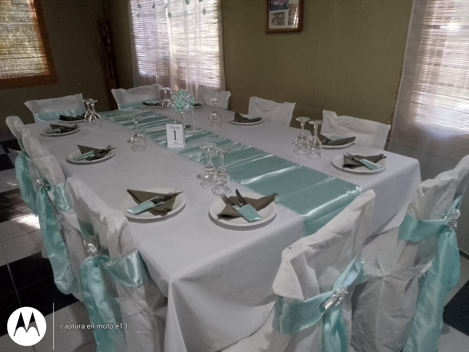 Una larga mesa rectangular para banquetes, puesta con mantelería blanca, caminos de mesa azul claro