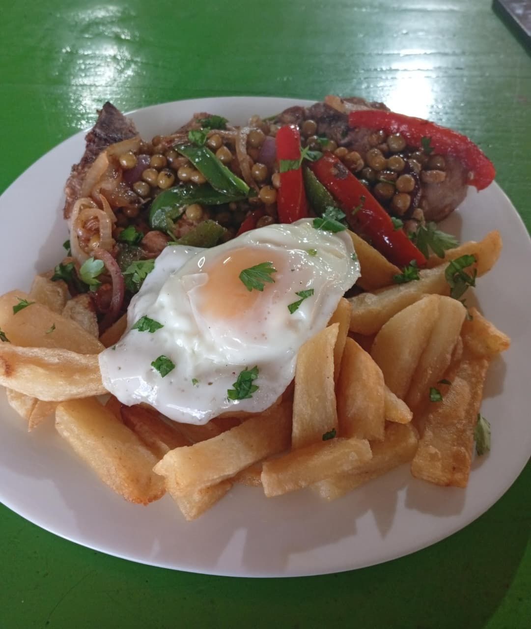 Un plato que consiste en un huevo frito sobre patatas fritas gruesas, cubierto con pimientos en rodajas