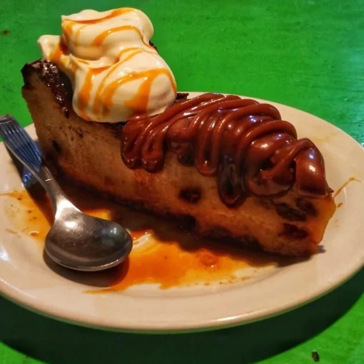 Una porción de tarta de queso con sirope de caramelo y nata montada, servida en un plato 