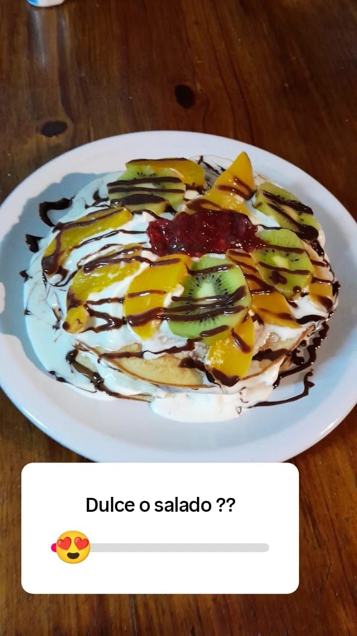 Una pila de panqueques cubiertos con crema batida, kiwi, duraznos, mermelada y sirope de chocolate