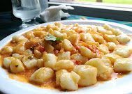 Primer plano de un plato blanco lleno de ñoquis de patata en una salsa de tomate ligera, servido sobre una mesa.