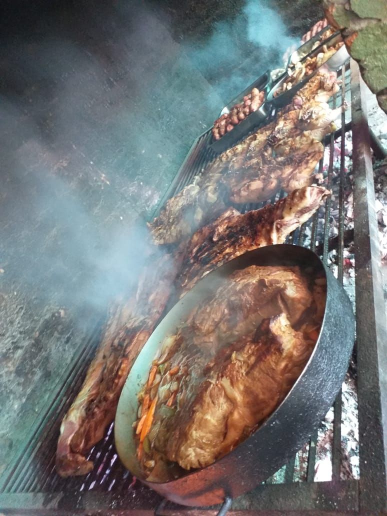 Una variedad de carnes y una sartén con comida cocinada chisporroteando sobre una parrilla de carbón